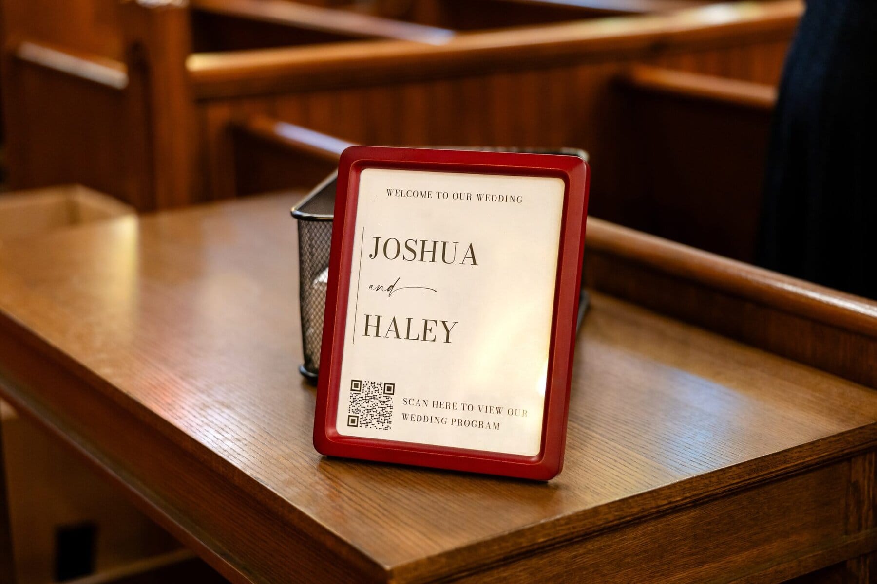 Wedding At the Transfiguration of the Lord Parish 33 A framed wedding sign on a wooden bench reads “Joshua and Haley” with a QR code for their Transfiguration of the Lord Parish wedding program.