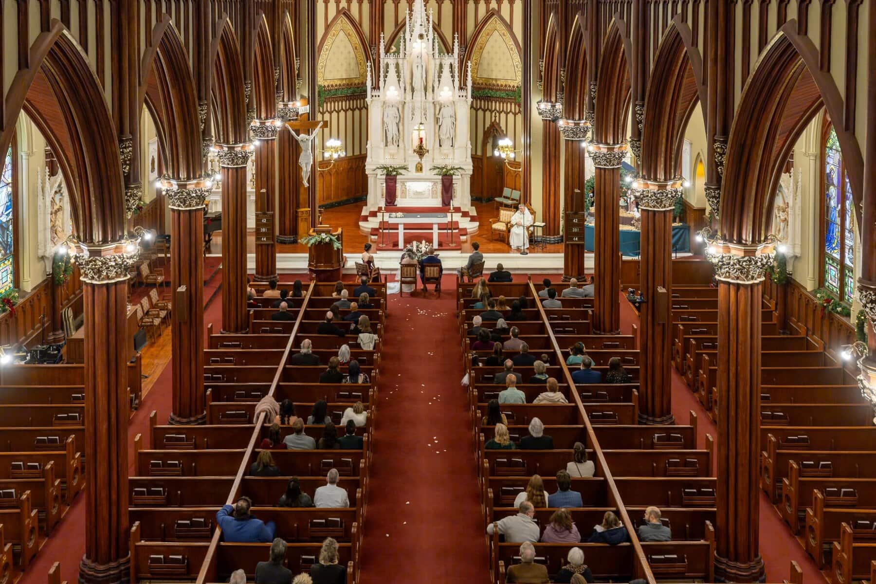 Wedding At the Transfiguration of the Lord Parish 53 A view from above of a wedding at Transfiguration of the Lord Parish, with guests seated in pews facing the altar during the ceremony.