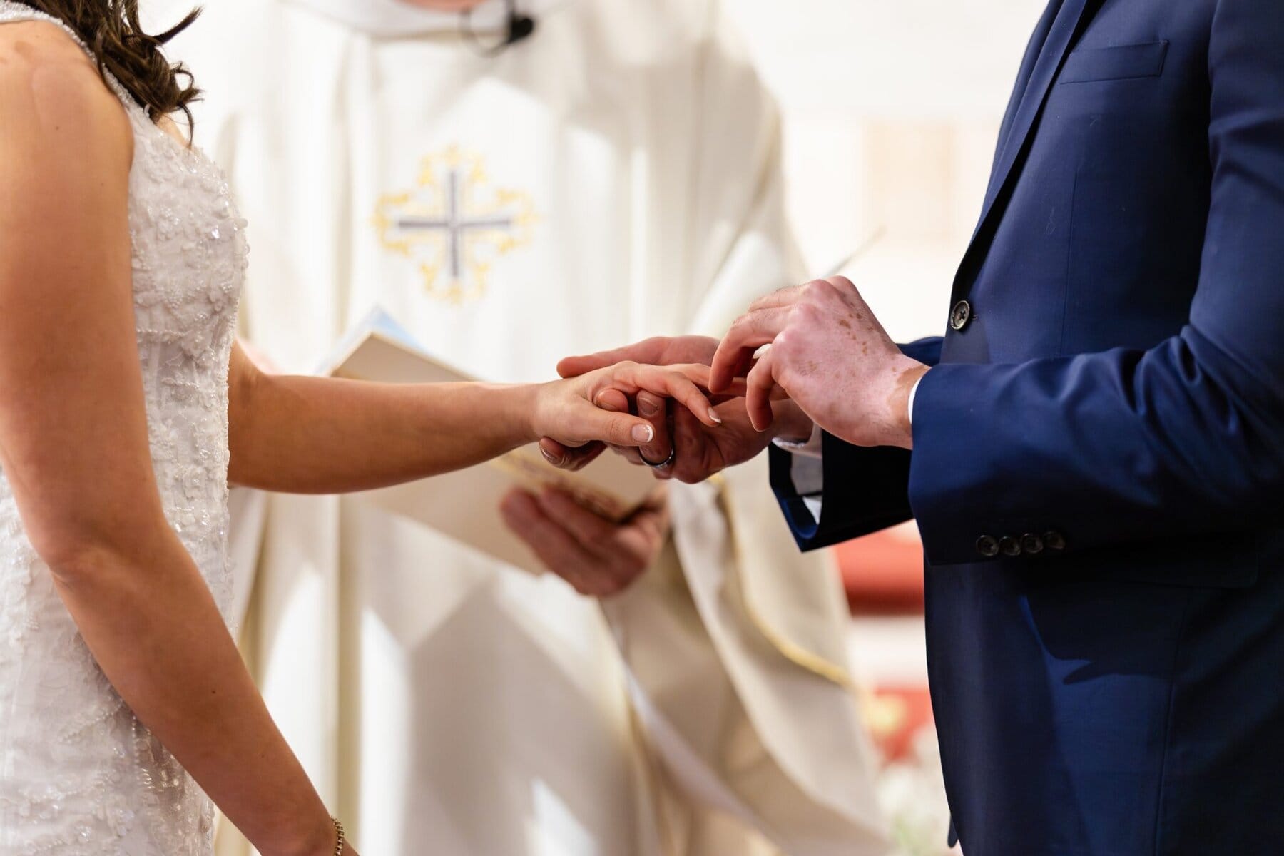 Wedding At the Transfiguration of the Lord Parish 44 A person in a blue suit places a ring on a woman's finger during a wedding ceremony at Transfiguration of the Lord Parish.