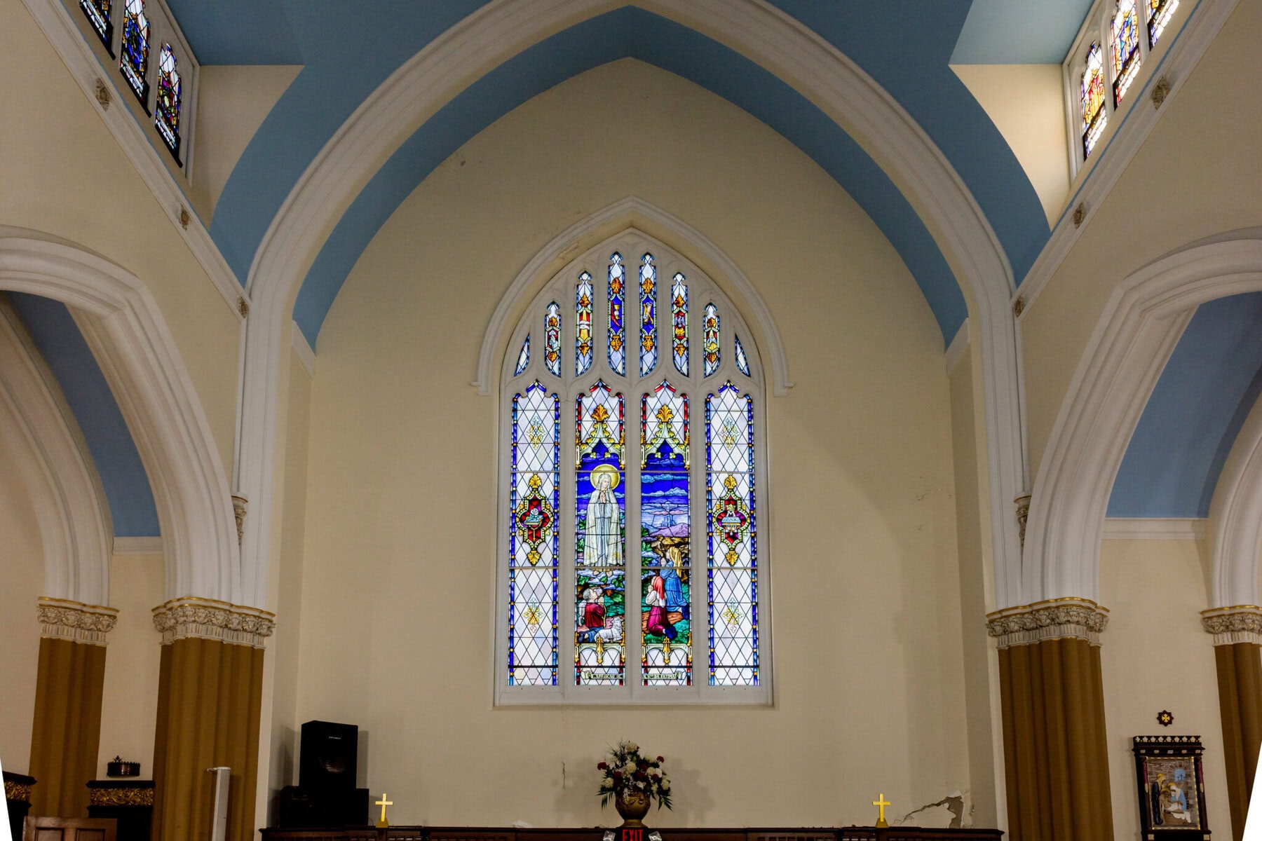 Wedding At Santo Christo Parish in Fall River 6 A church interior at Santo Christo Parish in Fall River, featuring stained glass windows, arched ceilings, and a wedding floral arrangement on the altar.