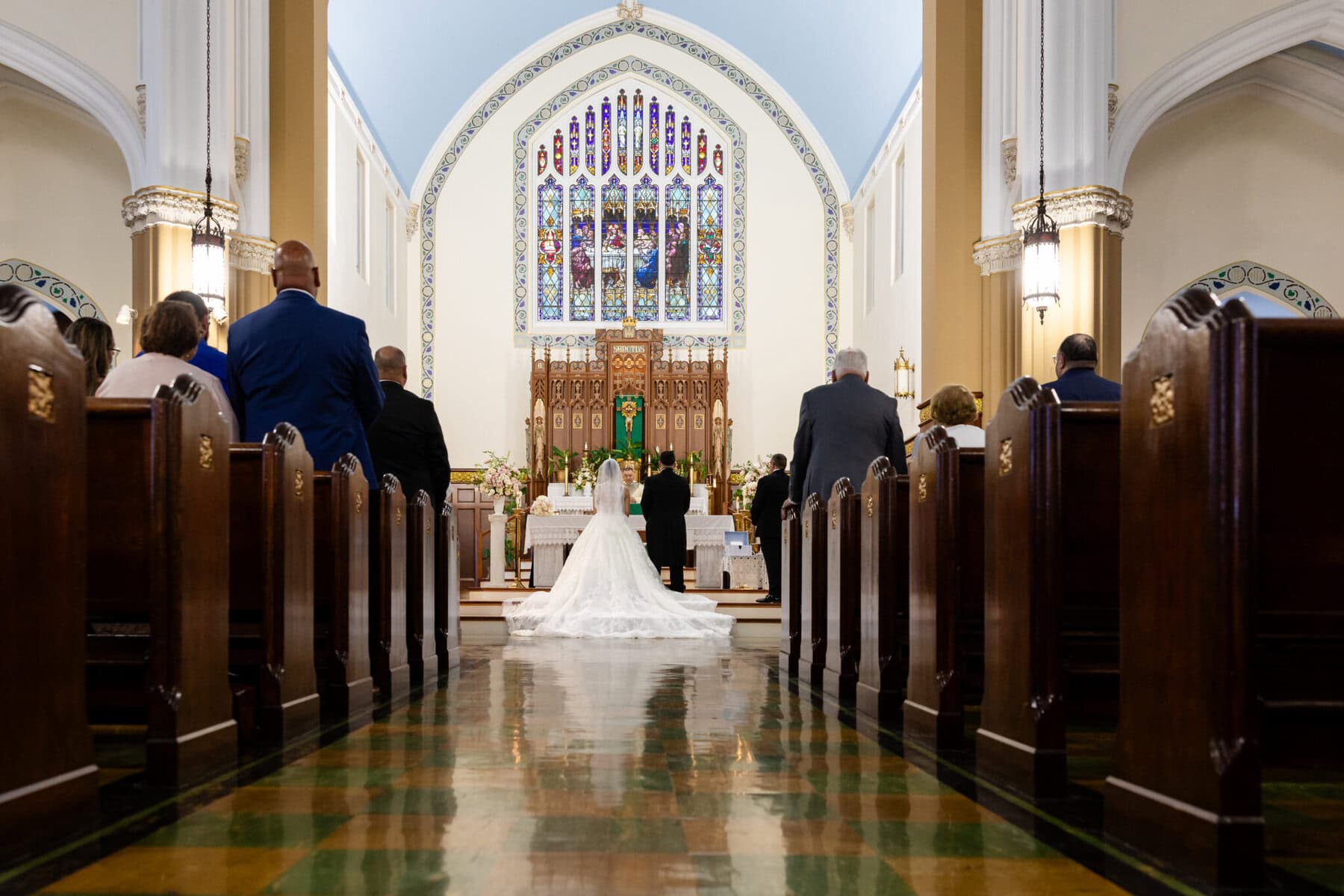 Wedding At Santo Christo Parish in Fall River 23 A bride and groom kneel at the altar of Santo Christo Parish in Fall River during a wedding, guests seated in pews on either side.