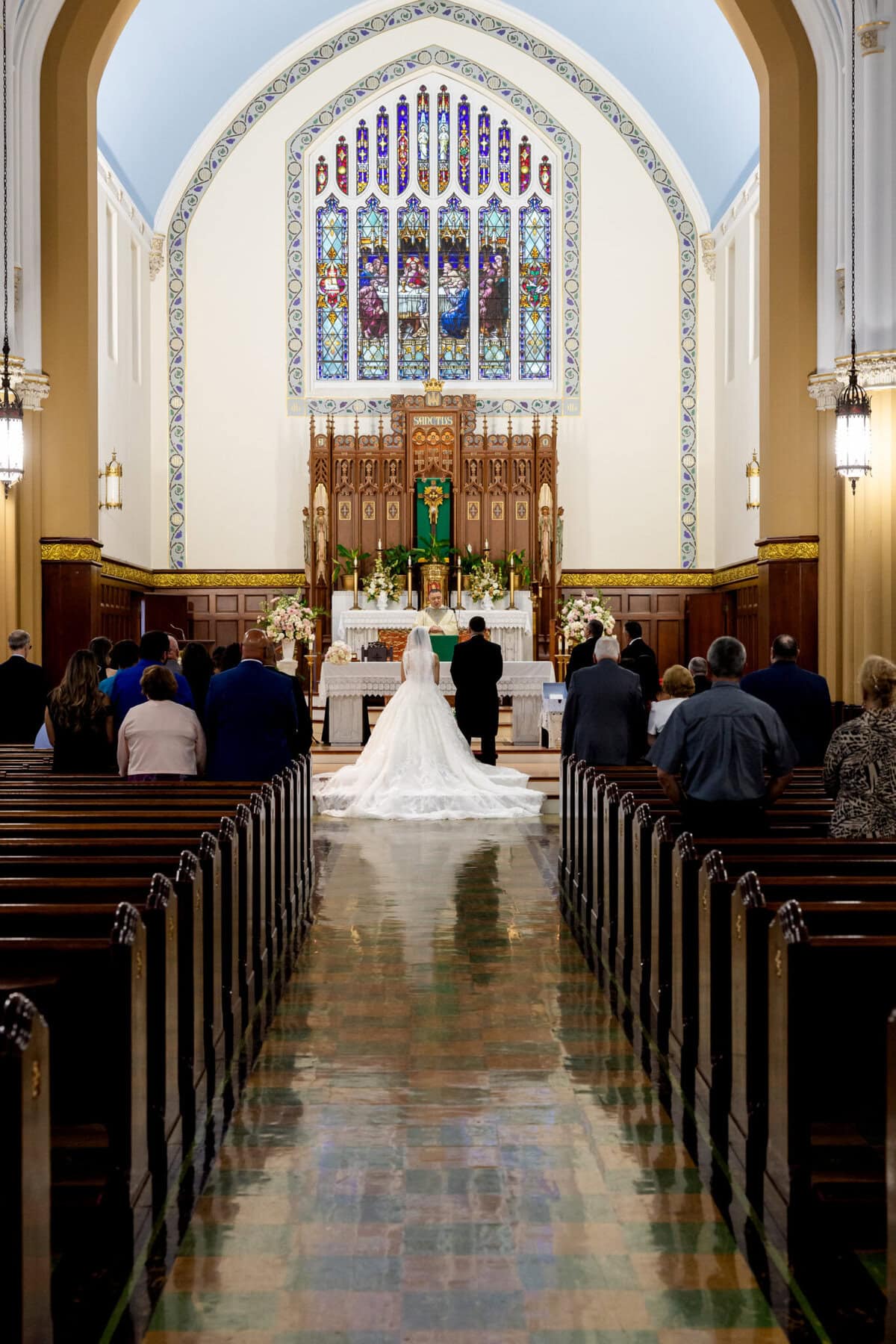 Wedding At Santo Christo Parish in Fall River 24 A bride and groom stand at the altar in Santo Christo Parish, Fall River, as wedding guests watch from pews on either side of the aisle.