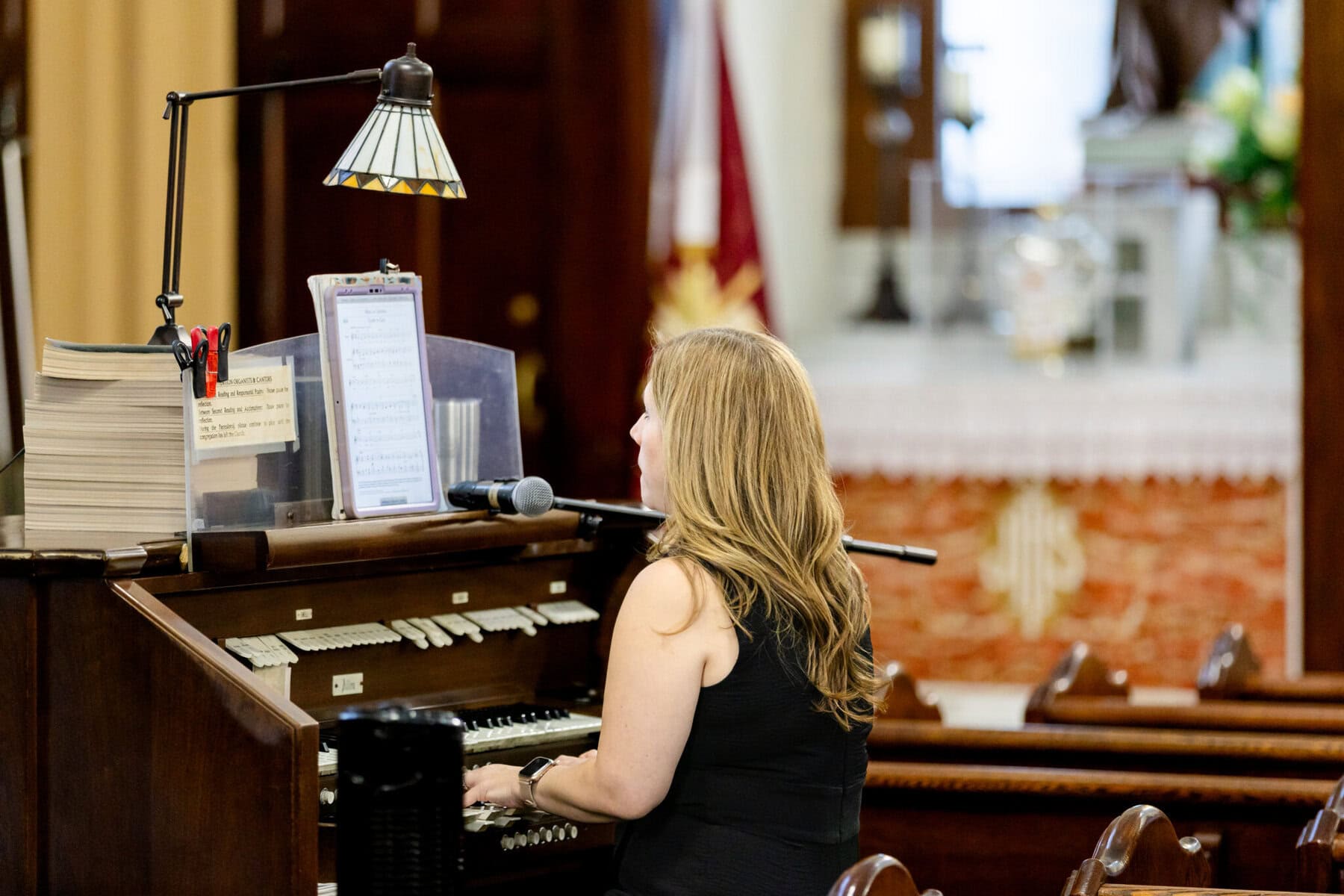 Wedding At Santo Christo Parish in Fall River 26 A woman with long blonde hair plays an organ at Santo Christo Parish in Fall River, reading sheet music, with a microphone nearby.