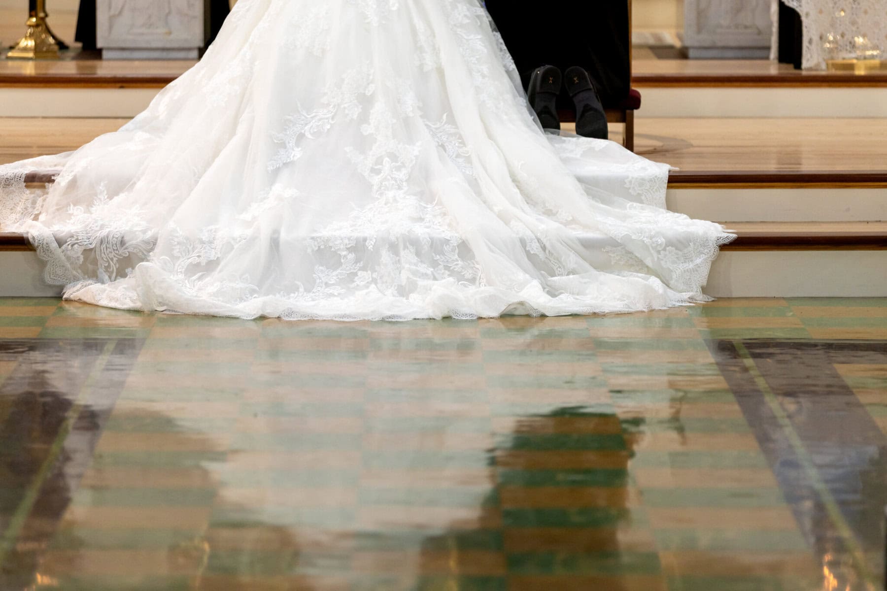 Wedding At Santo Christo Parish in Fall River 32 A white lace wedding dress trails down the altar steps at Santo Christo Parish, with the bride and another seated, only their legs visible.
