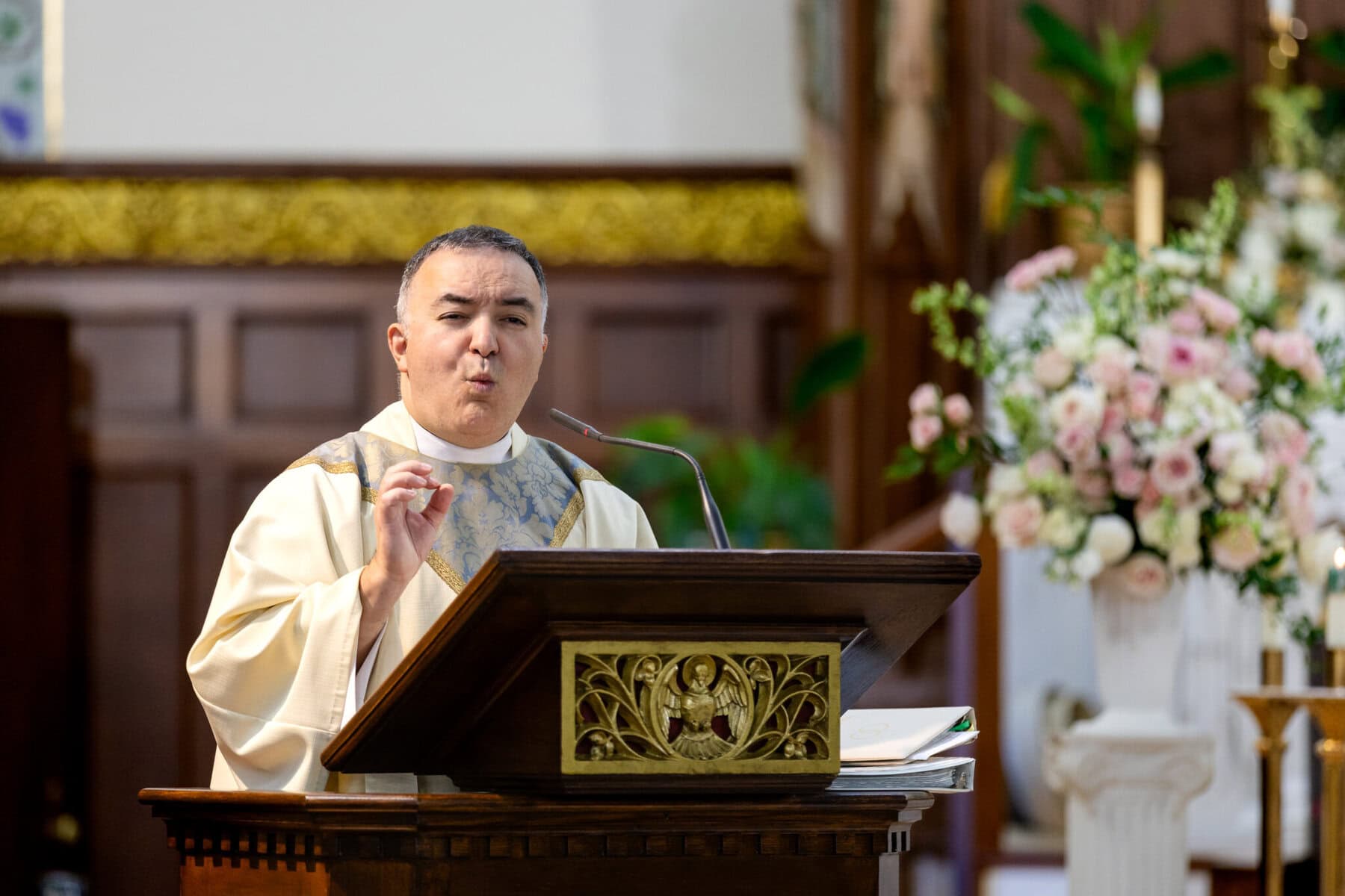 Wedding At Santo Christo Parish in Fall River 36 A priest in ceremonial robes speaks at a pulpit inside Santo Christo Parish, with flowers and candles visible in the Fall River church.