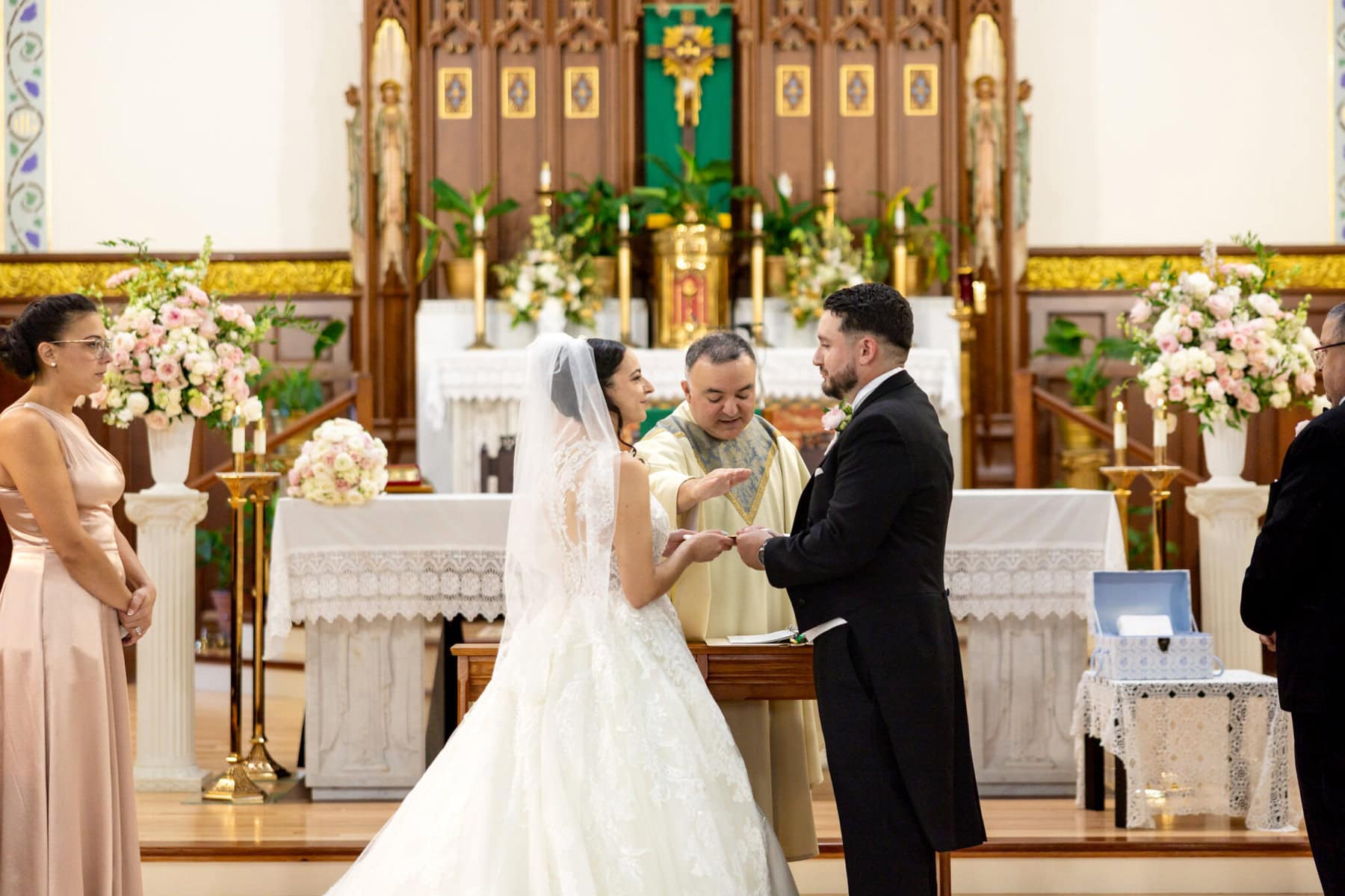 Wedding At Santo Christo Parish in Fall River 40 A bride and groom exchange rings at the altar during a Santo Christo Parish Wedding in Fall River, with a priest and two attendants nearby.