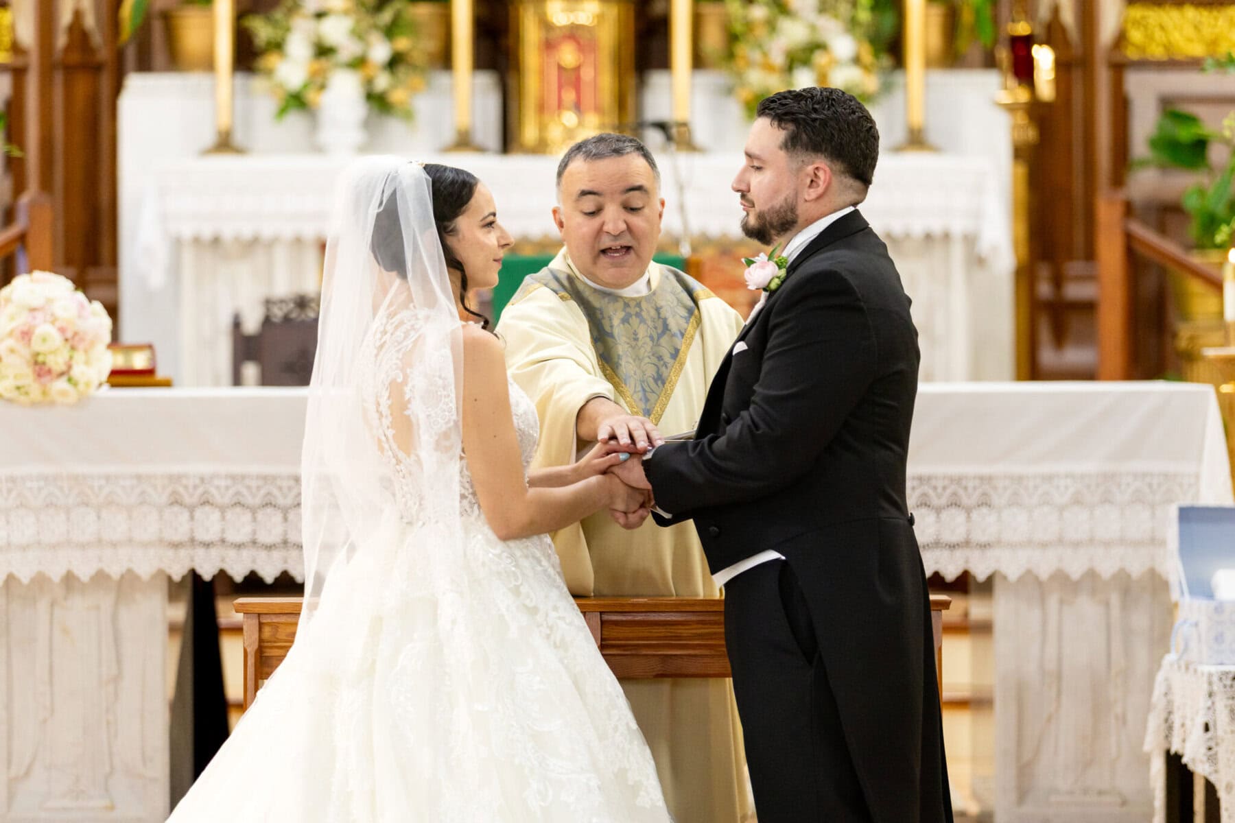 Wedding At Santo Christo Parish in Fall River 41 A bride and groom hold hands at the altar as a priest conducts a wedding at Santo Christo Parish in Fall River.