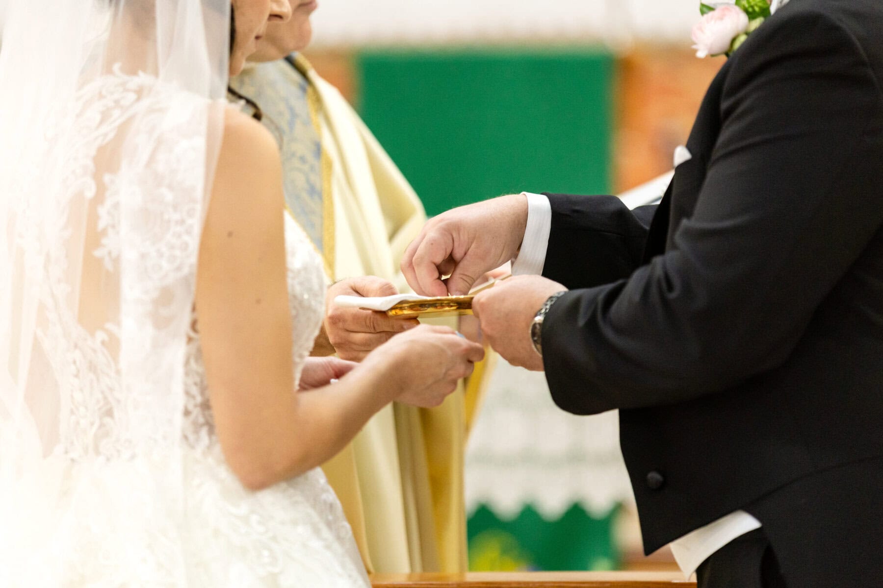 Wedding At Santo Christo Parish in Fall River 42 A bride and groom exchange rings during a wedding ceremony at Santo Christo Parish, with a person in religious attire standing beside them.