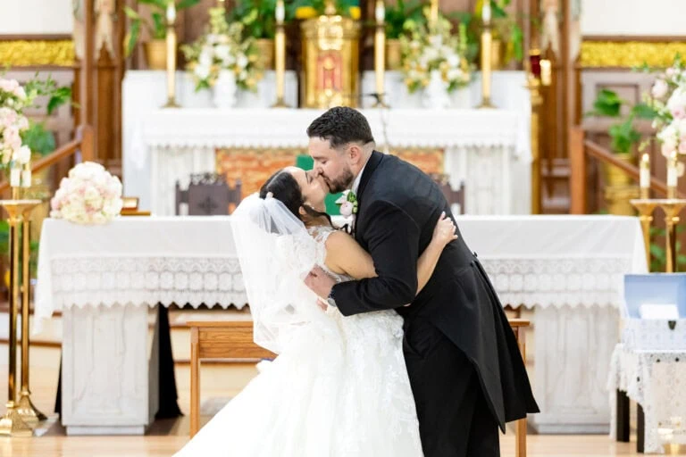 A bride and groom kiss at the altar during their Fall River wedding at the beautifully decorated Santo Christo Parish.