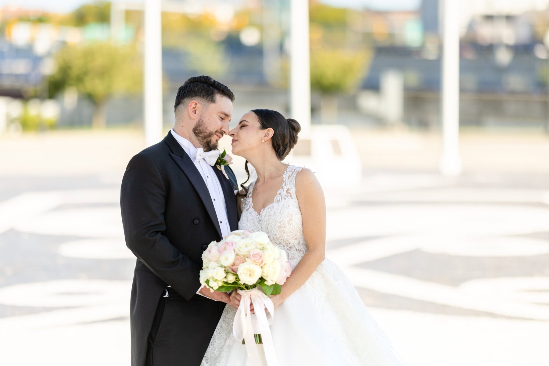 Wedding Photos at City Gates Plaza in Fall River 8 A bride and groom share a kiss outdoors at City Gates Plaza, the bride holding a bouquet of white and pink flowers.