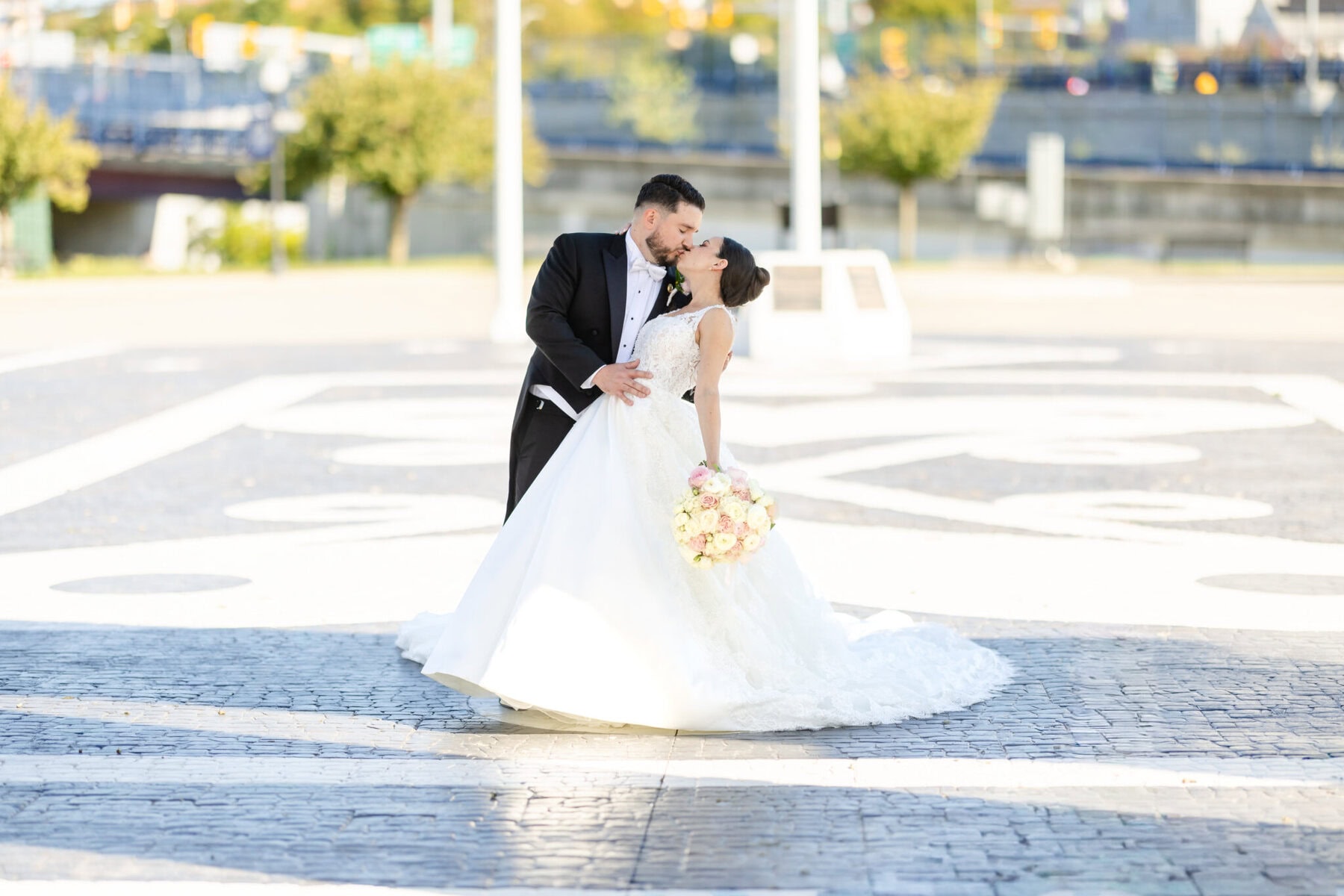 Wedding Photos at City Gates Plaza in Fall River 6 A bride and groom in formal attire share a kiss outdoors at City Gates Plaza; the bride holds a bouquet of flowers. Wedding Photos, Fall River.