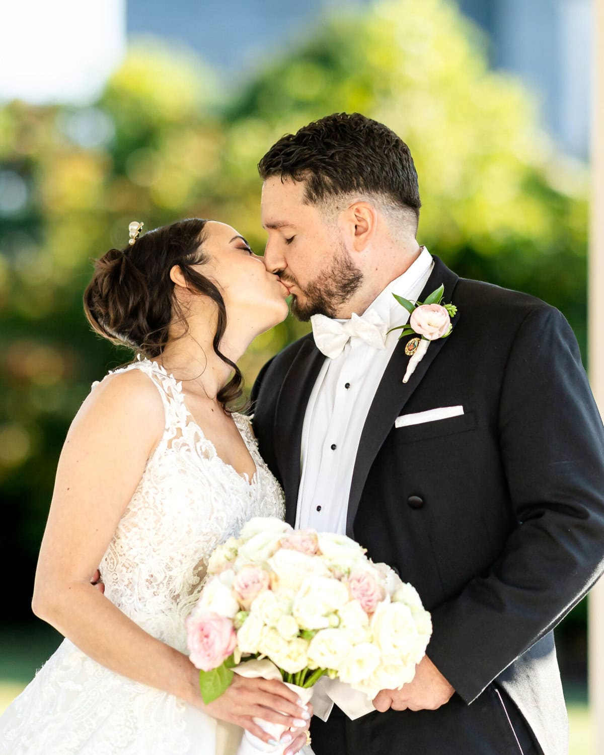 Wedding Photos at Roseland Nursery 2 A bride and groom in formal attire kiss outdoors at Roseland Nursery, with the bride holding a bouquet in this stunning wedding photography moment.