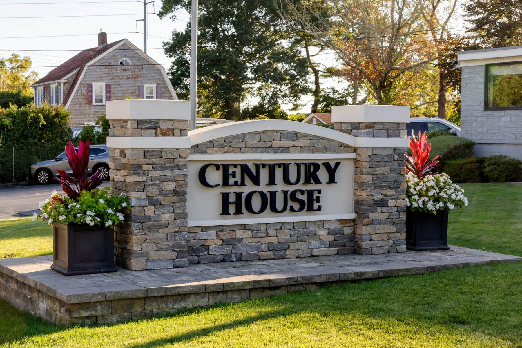 Wedding Reception at The Century House in Acushnet 20 A stone sign reading "Century House" sits on an Acushnet lawn, bordered by two planters with red and white flowers.