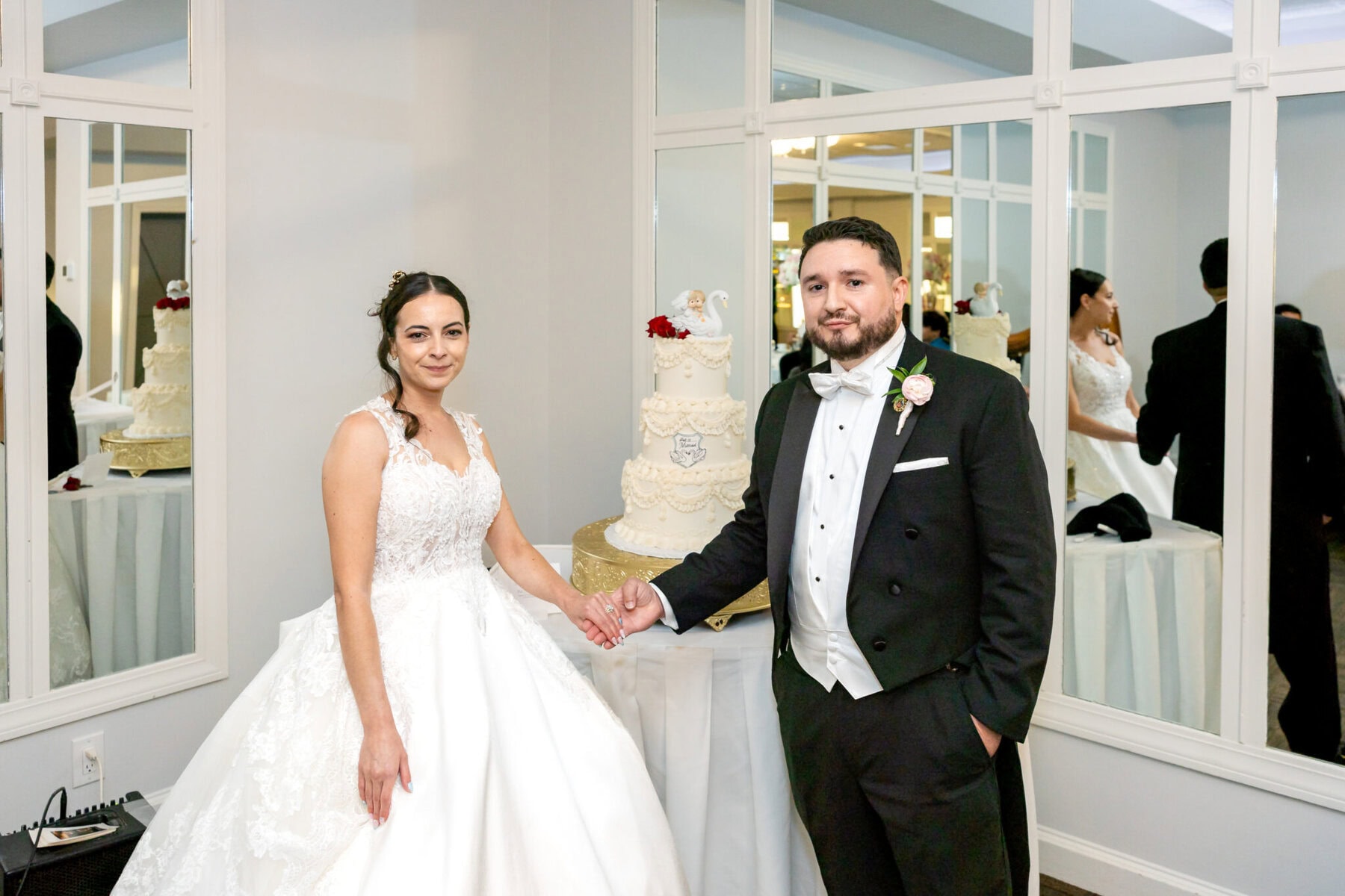 Wedding Reception at The Century House in Acushnet 14 A bride and groom stand together, holding hands beside a decorated cake at their Century House wedding reception in Acushnet.