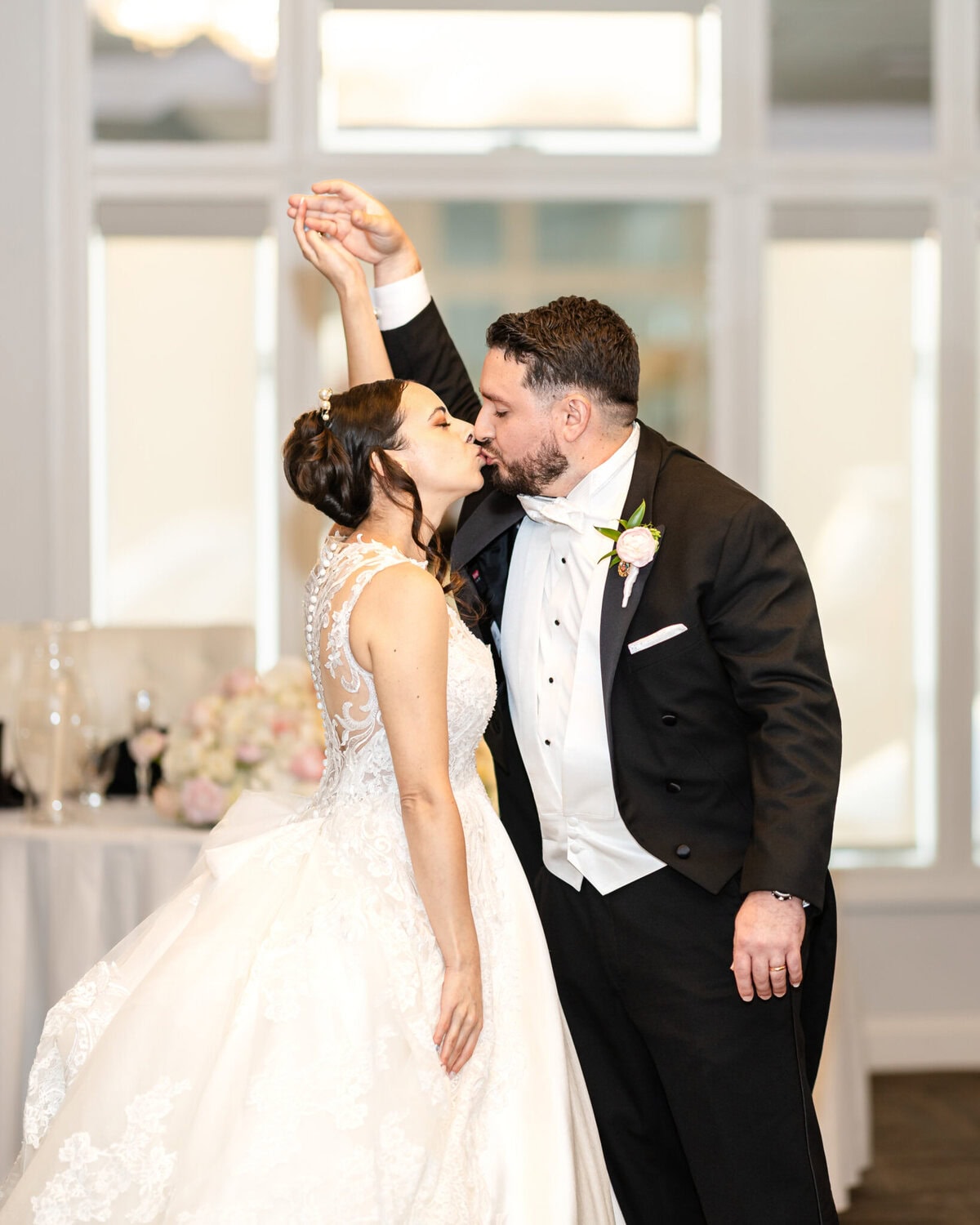 Wedding Reception at The Century House in Acushnet 19 A bride and groom in formal wedding attire share a kiss at The Century House in Acushnet, with flowers and a window in the background.