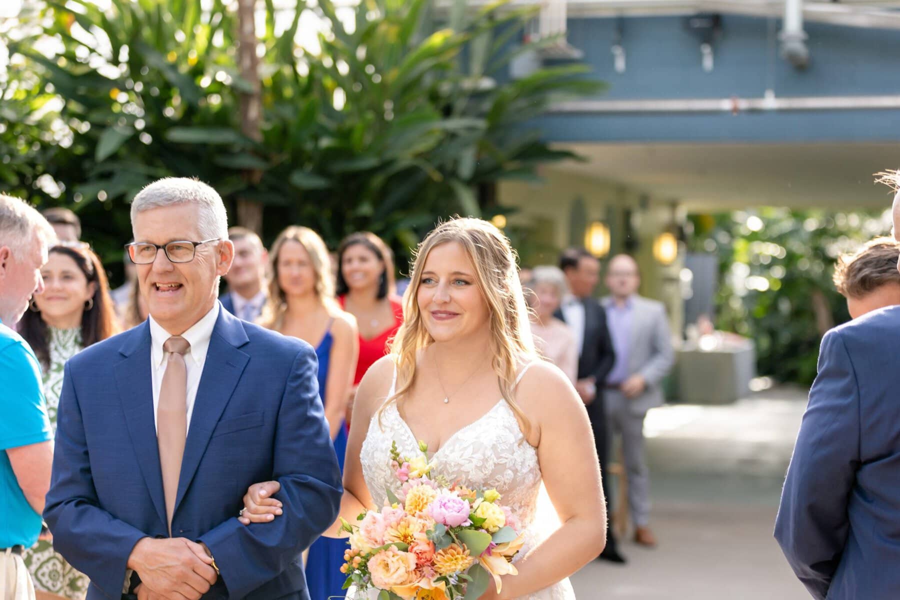 Stunning Wedding at the Roger Williams Botanical Gardens 25 A bride holding a bouquet walks arm-in-arm with an older man down the aisle at a Roger Williams Botanical Gardens wedding.