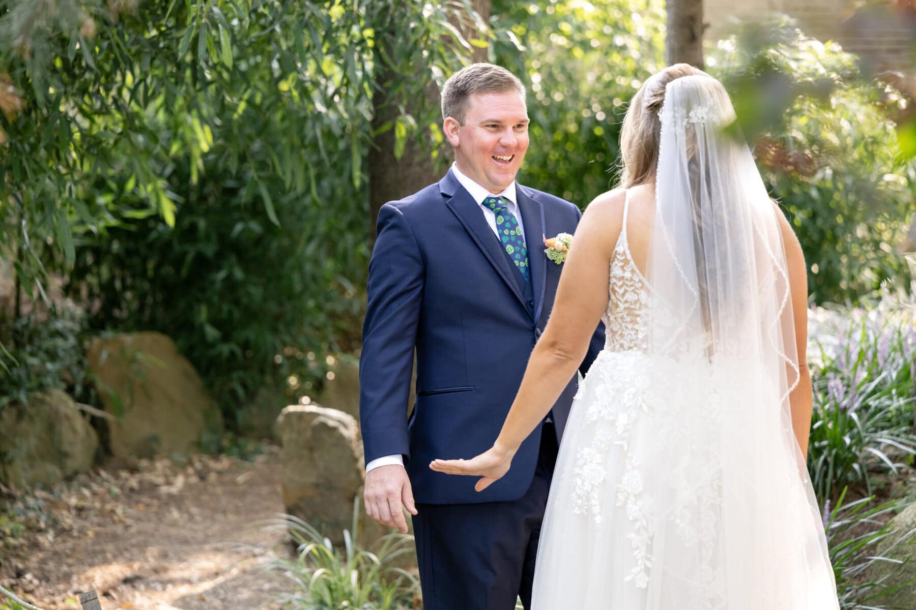 Stunning Wedding at the Roger Williams Botanical Gardens 9 A bride and groom stand facing each other outdoors, smiling, surrounded by sunlight and greenery at Roger Williams Botanical Gardens.