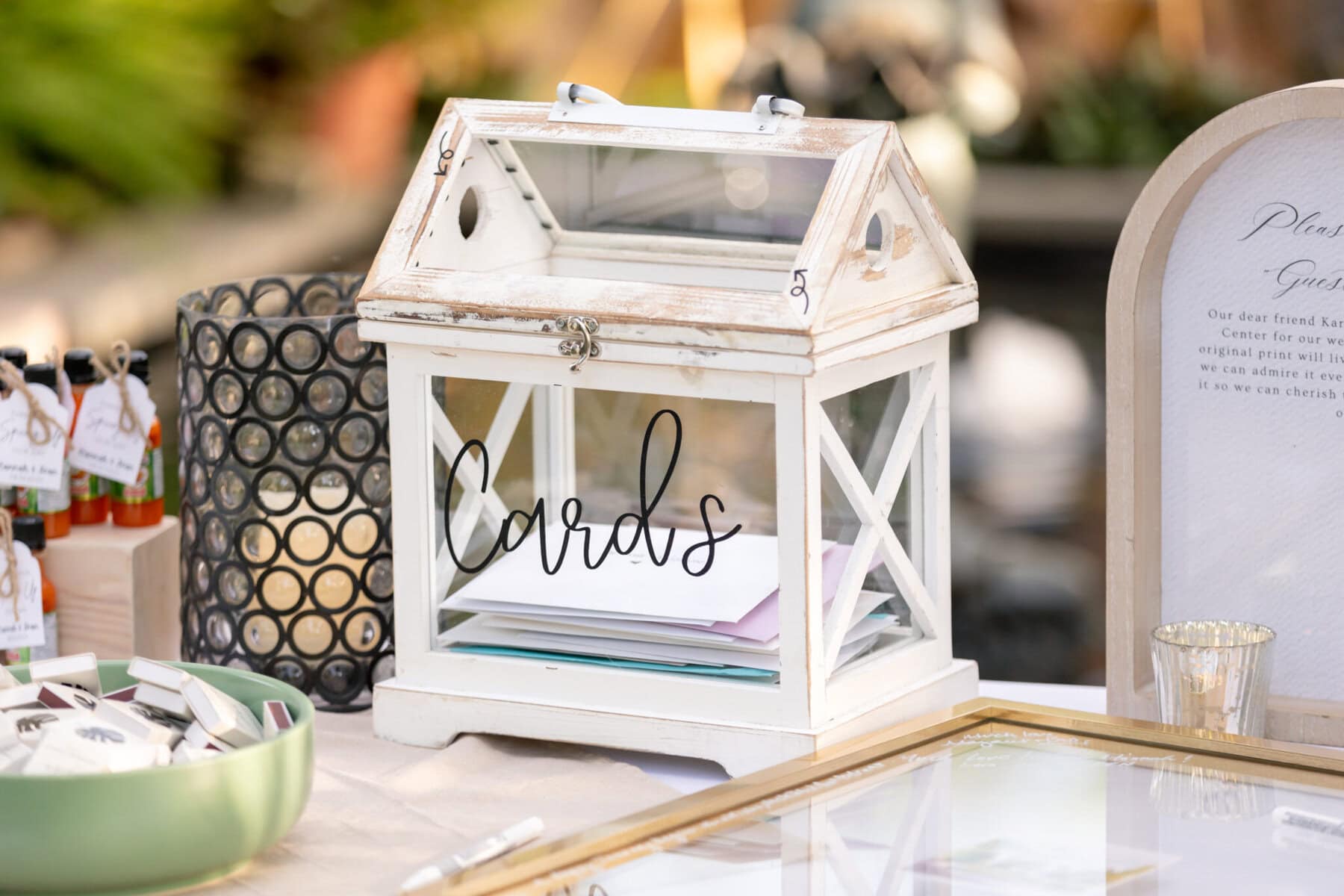 Stunning Wedding at the Roger Williams Botanical Gardens 63 A glass and white wooden card box labeled "Cards" sits on a table at a wedding in Roger Williams Botanical Gardens.