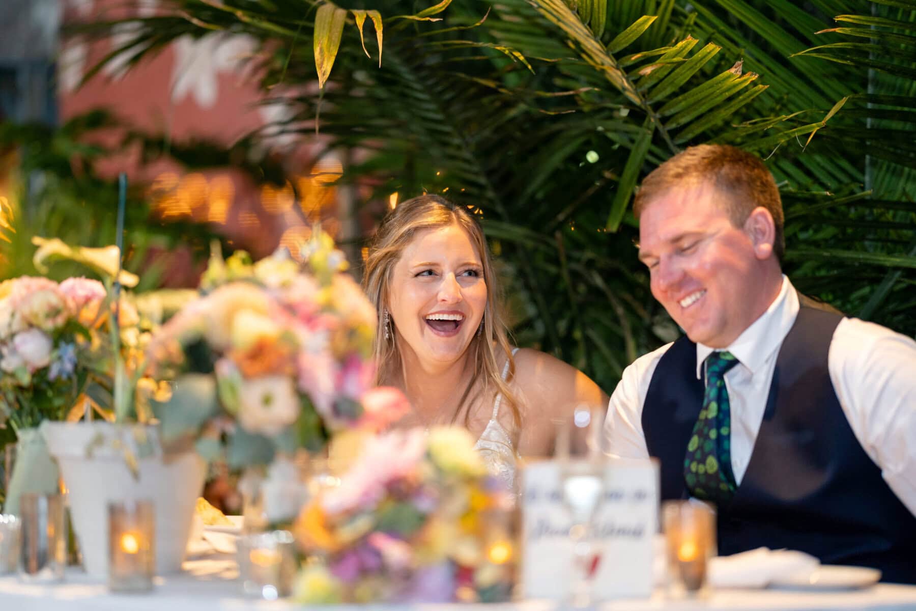 Stunning Wedding at the Roger Williams Botanical Gardens 74 A smiling couple laughs at their wedding table, surrounded by flowers and candles at Roger Williams Botanical Gardens.