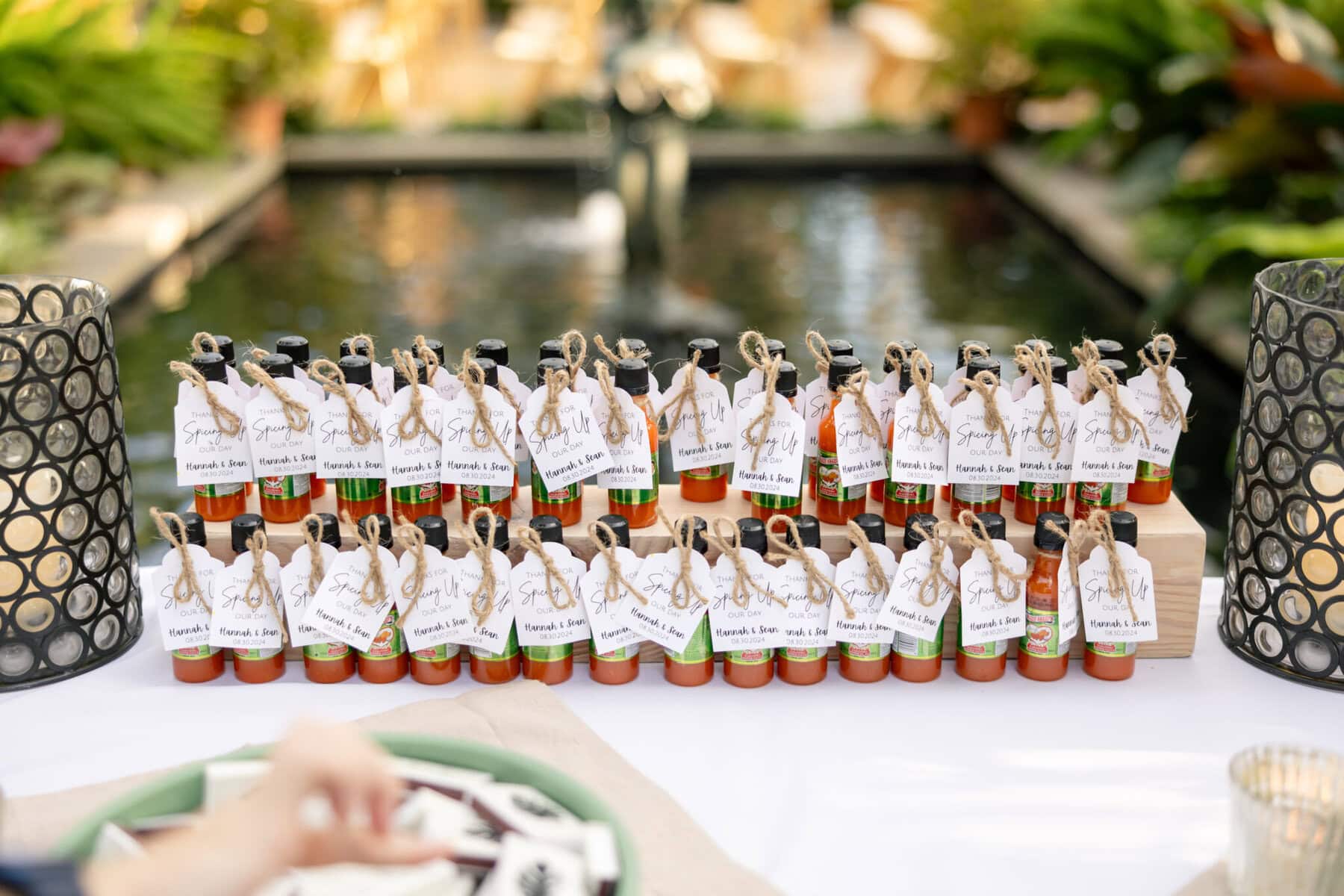 Stunning Wedding at the Roger Williams Botanical Gardens 75 Small bottles with personalized tags are arranged by a pond at a Roger Williams Botanical Gardens wedding, flanked by lanterns and greenery.