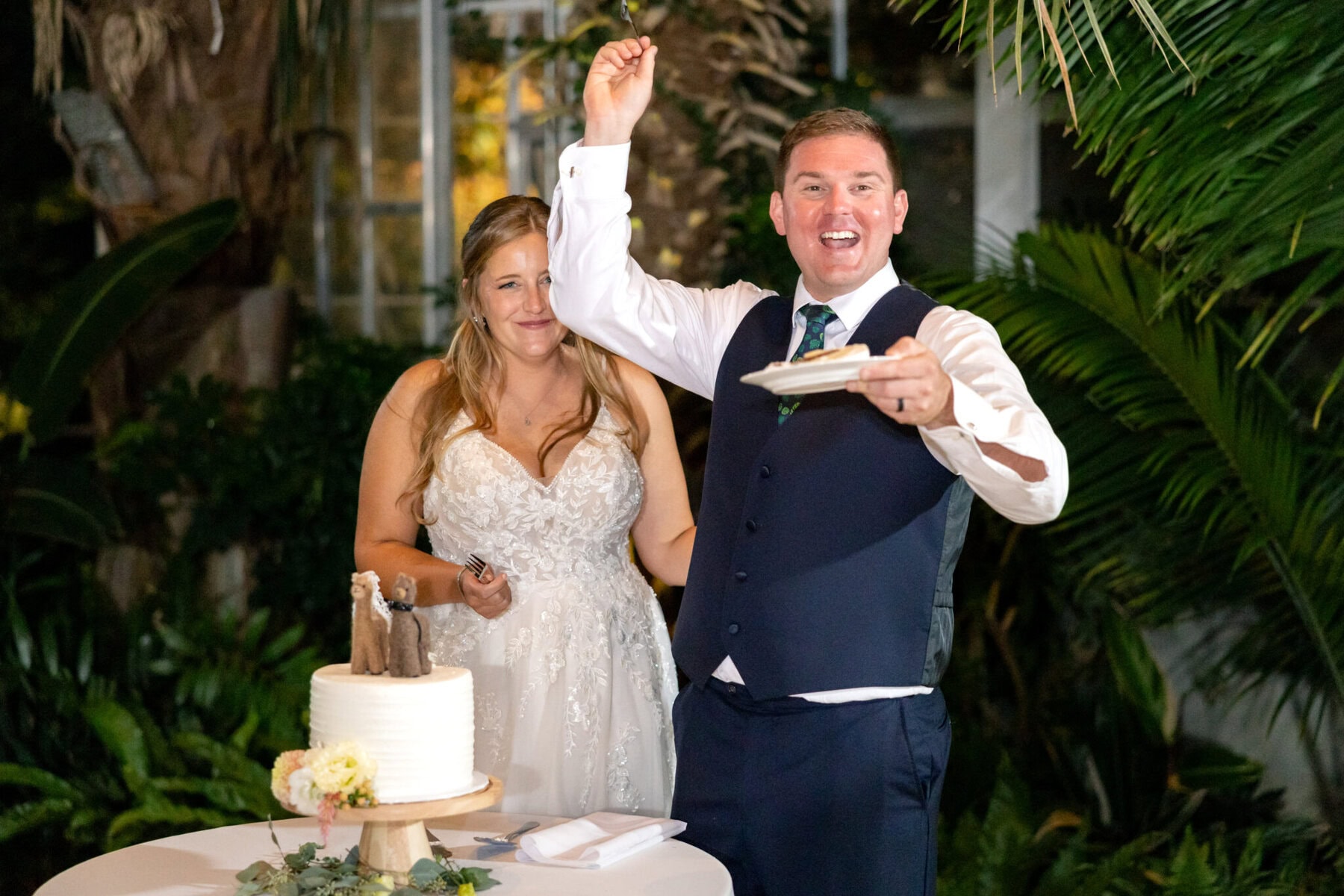 Stunning Wedding at the Roger Williams Botanical Gardens 81 A man in a vest raises his arm with a plate, standing by his bride at their wedding in the Roger Williams Botanical Gardens.