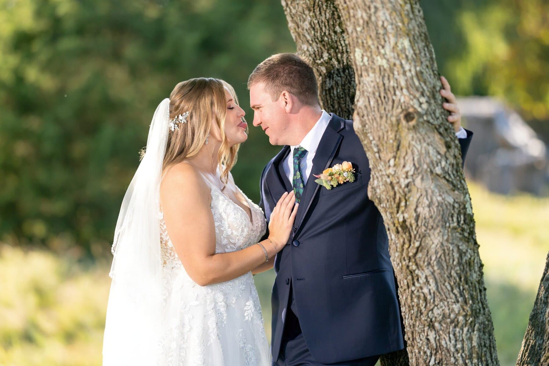 Stunning Wedding at the Roger Williams Botanical Gardens 103 A bride and groom stand closely together outdoors by a tree at Roger Williams Botanical Gardens, gazing at each other in wedding attire.