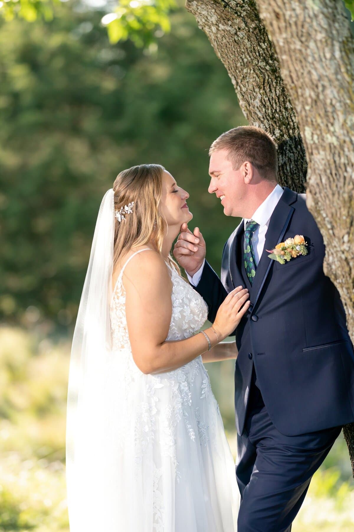 Stunning Wedding at the Roger Williams Botanical Gardens 105 A bride and groom stand close together outdoors by a tree at Roger Williams Botanical Gardens, smiling on their wedding day.