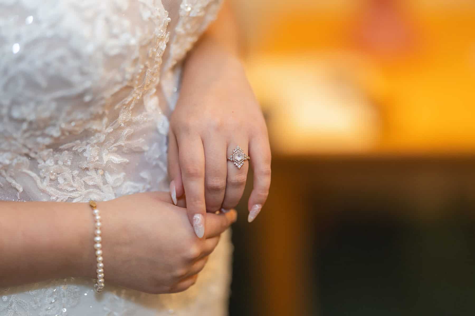Wedding at the Springfield Elks lodge 5 A bride in a lace wedding dress shows her diamond engagement ring and pearl bracelet at a Springfield wedding, hands gently clasped, softly blurred background.
