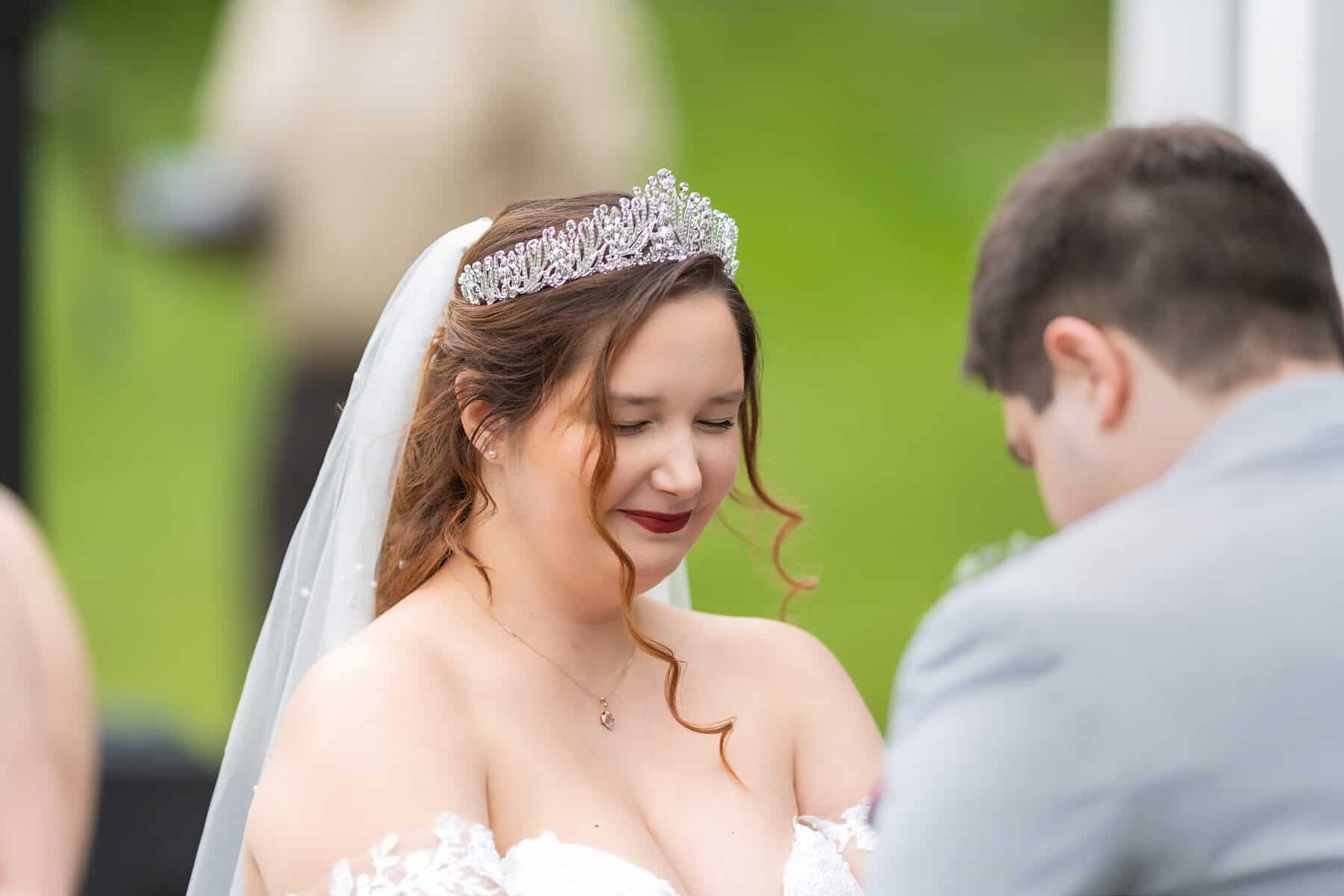 Wedding at the Springfield Elks lodge 19 A bride in a tiara and veil, eyes closed and smiling gently, stands facing her groom in a light gray suit at their Springfield wedding ceremony.