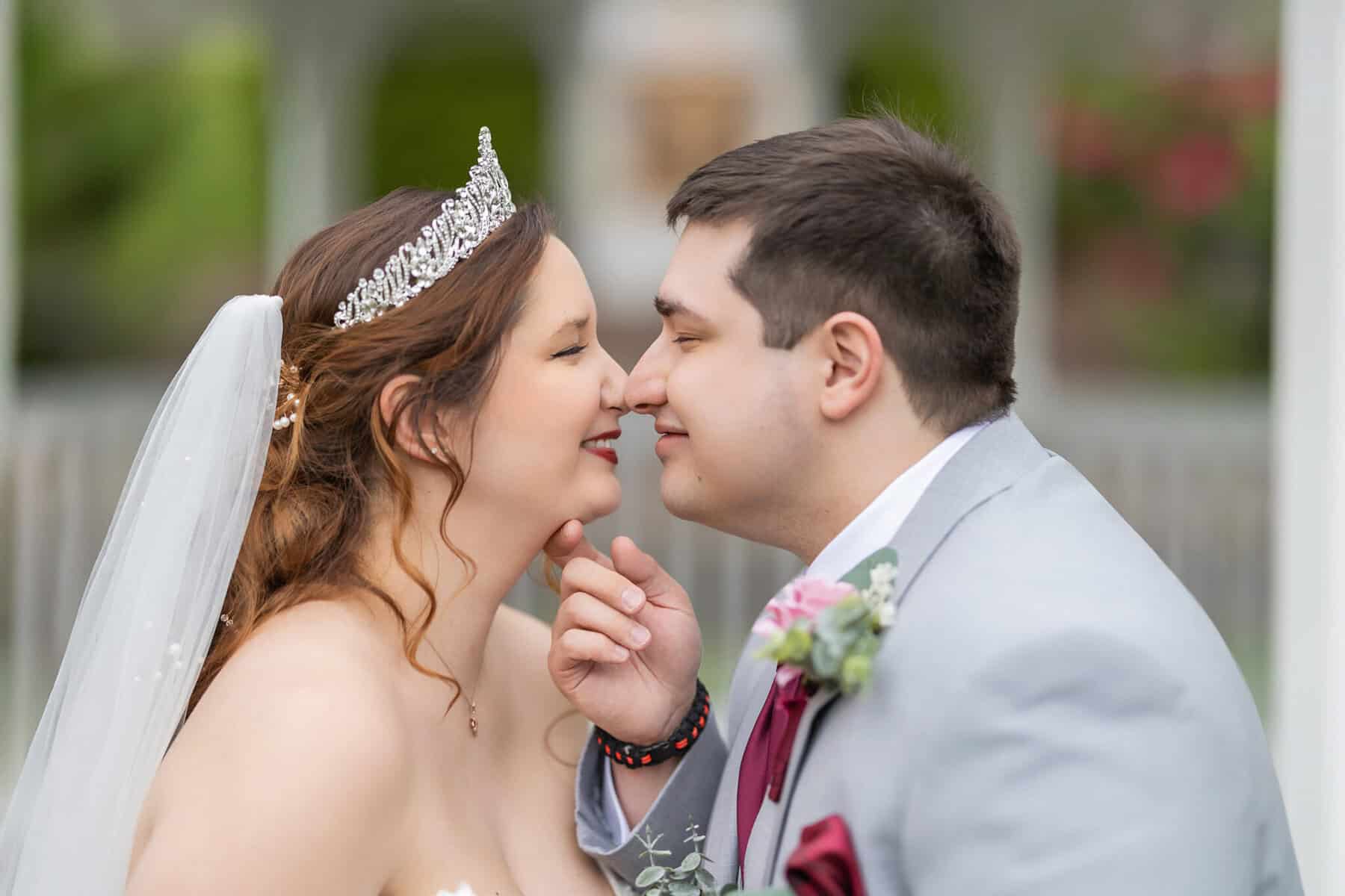 Wedding at the Springfield Elks lodge 35 A bride in a tiara and veil gently touches noses with the groom in a light gray suit; both smile softly, sharing a tender moment at their Springfield wedding outdoors.