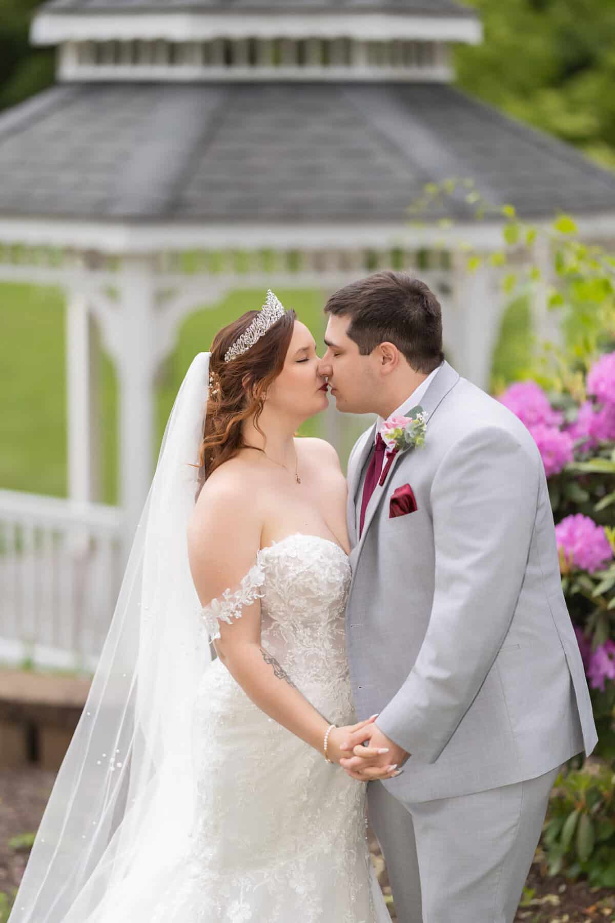 Wedding at the Springfield Elks lodge 43 A bride and groom kiss in front of a white gazebo at the Springfield Elks Lodge, holding hands—a charming wedding moment in elegant attire.