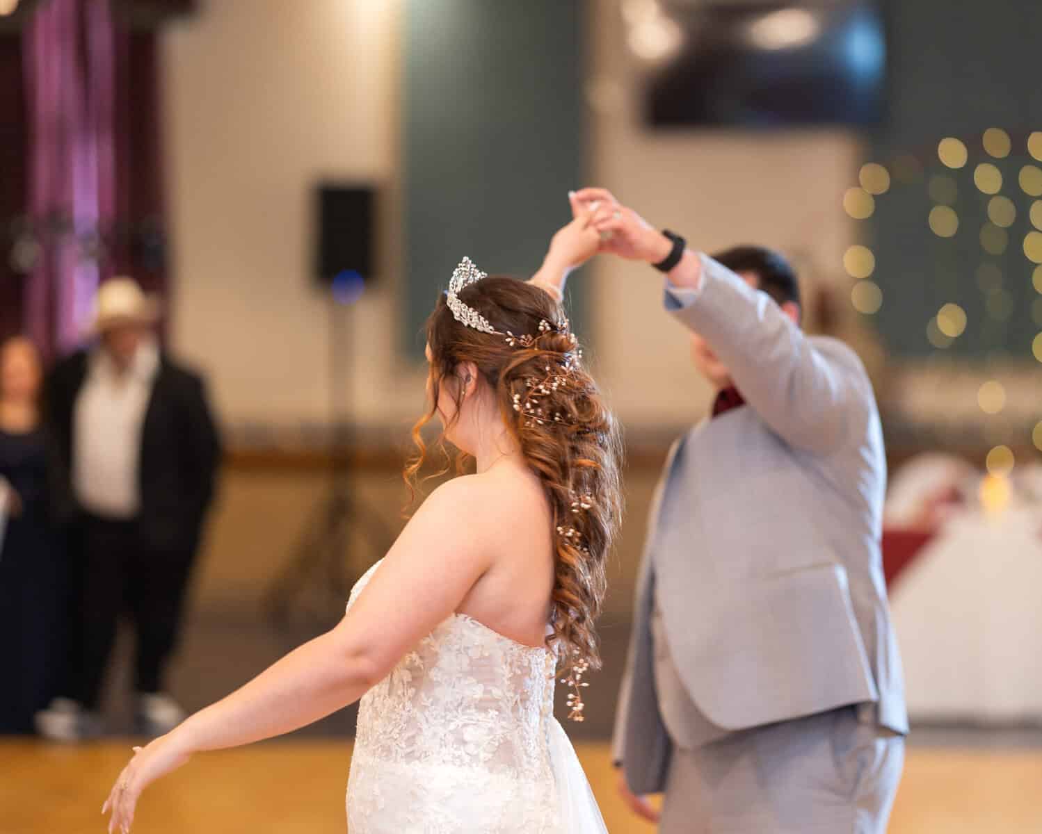 Wedding at the Springfield Elks lodge 61 A bride in a white lace dress and tiara dances with her groom at their Springfield wedding; her hair is adorned with delicate accessories, and the Elks Lodge background is softly blurred.