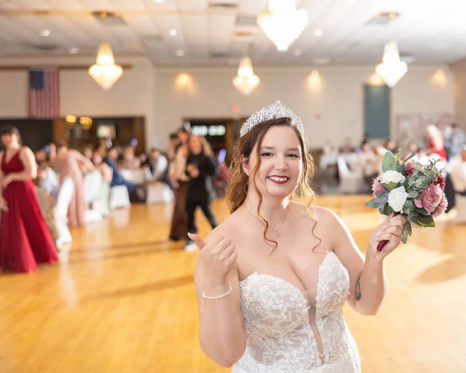 Wedding at the Springfield Elks lodge 75 A smiling bride in a white lace wedding gown and tiara prepares to toss her bouquet at a Springfield Elks Lodge wedding, with guests and chandeliers visible in the decorated hall.