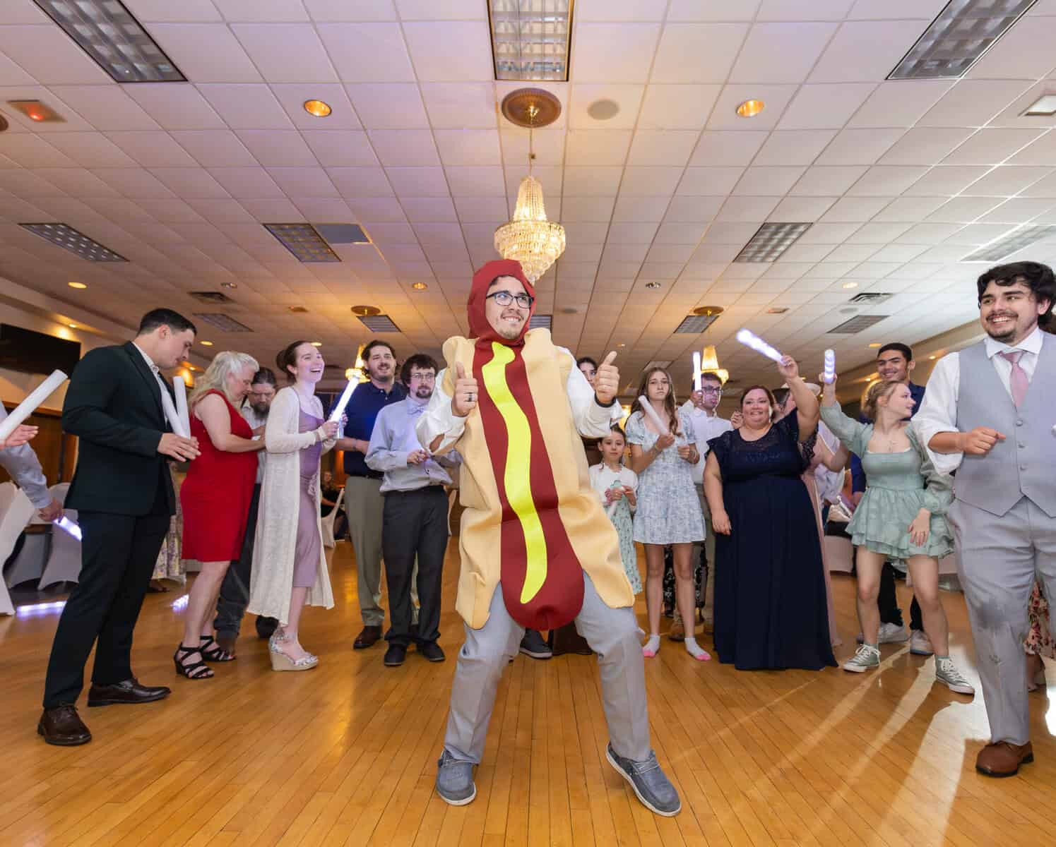 Wedding at the Springfield Elks lodge 84 A person in a hot dog costume poses with thumbs up on a dance floor at a lively Springfield wedding, surrounded by guests cheering at the Elks Lodge.