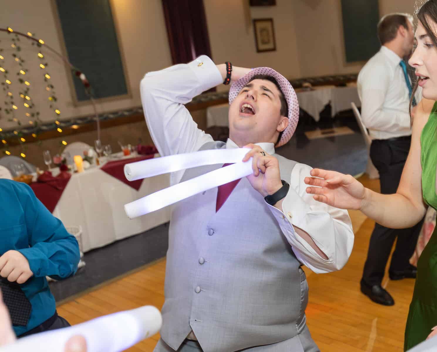 Wedding at the Springfield Elks lodge 86 A man in a gray vest and tie dances joyfully at an Elks Lodge wedding in Springfield, holding three glowing light sticks as others celebrate nearby in the decorated hall.