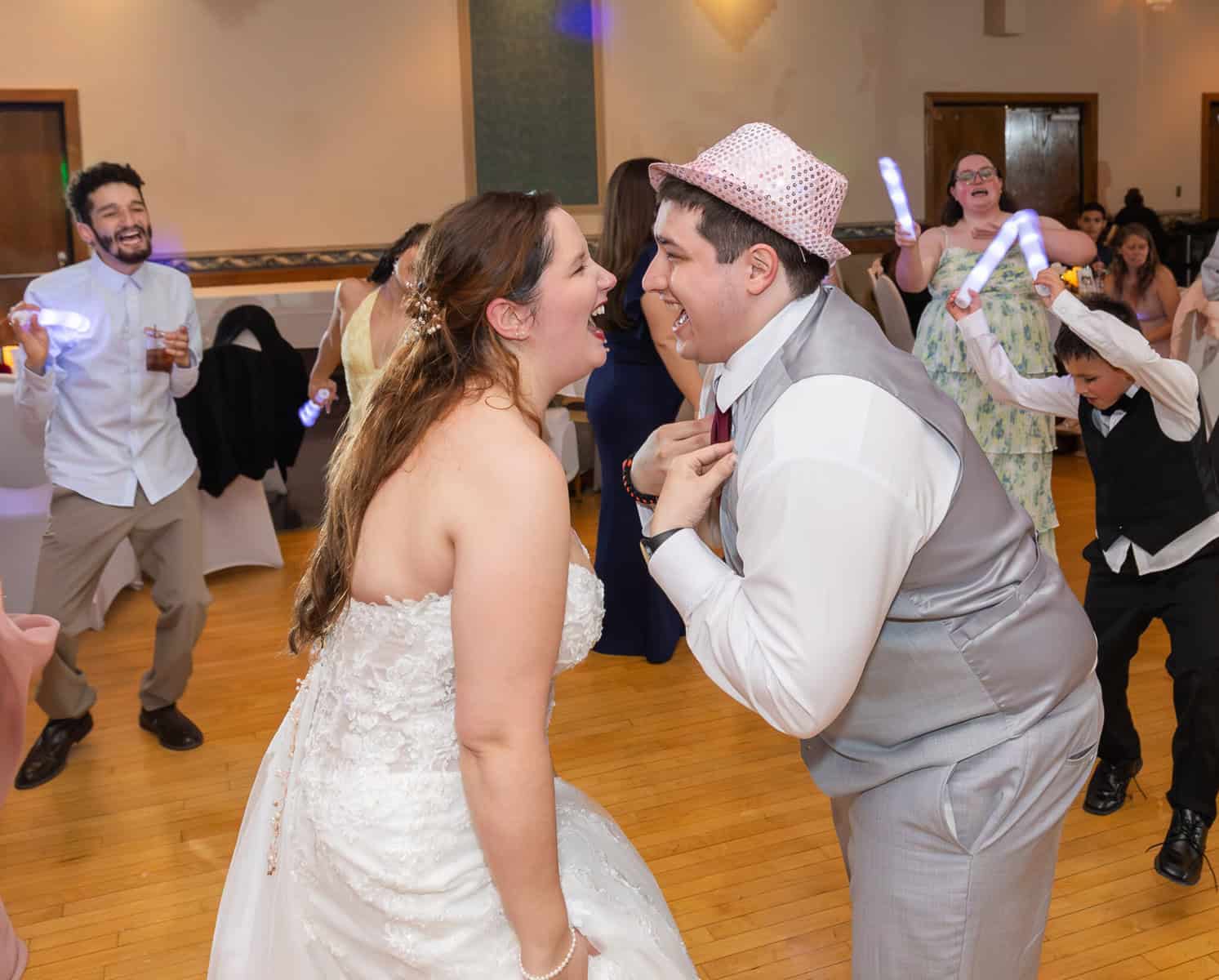 Wedding at the Springfield Elks lodge 88 A bride and groom laugh joyfully facing each other on the dance floor at their Springfield wedding, surrounded by cheering guests waving light sticks at the Elks Lodge.