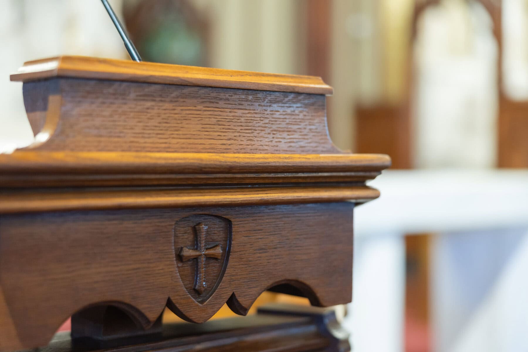 Wedding At St. Mary's Church in North Attleborough 17 A wooden lectern with a carved shield and cross design, photographed indoors at St. Mary's Church with a blurred background.