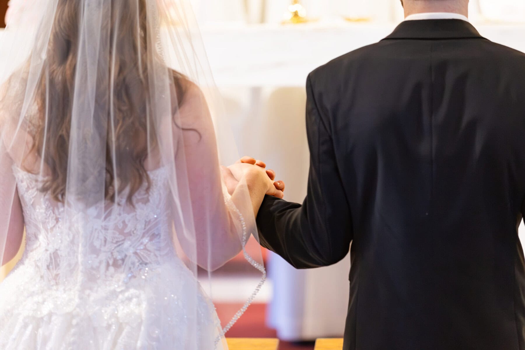 Wedding At St. Mary's Church in North Attleborough 41 A bride and groom stand side by side, holding hands at their North Attleborough wedding, facing away during the ceremony.
