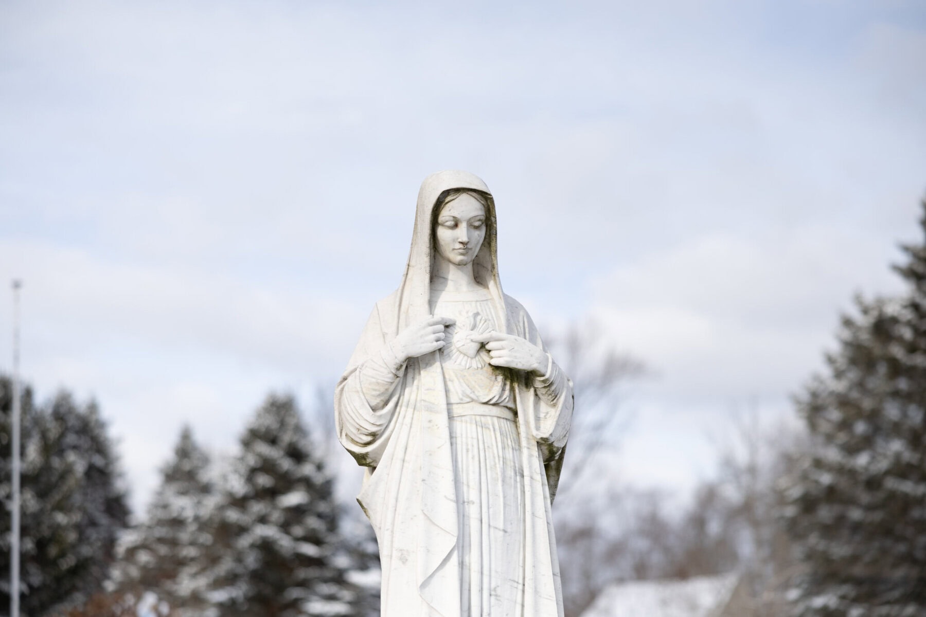 Wedding At the Transfiguration of the Lord Parish 4 A white statue of a veiled woman stands outdoors, evoking themes of the Transfiguration of the Lord amid trees and a cloudy sky.