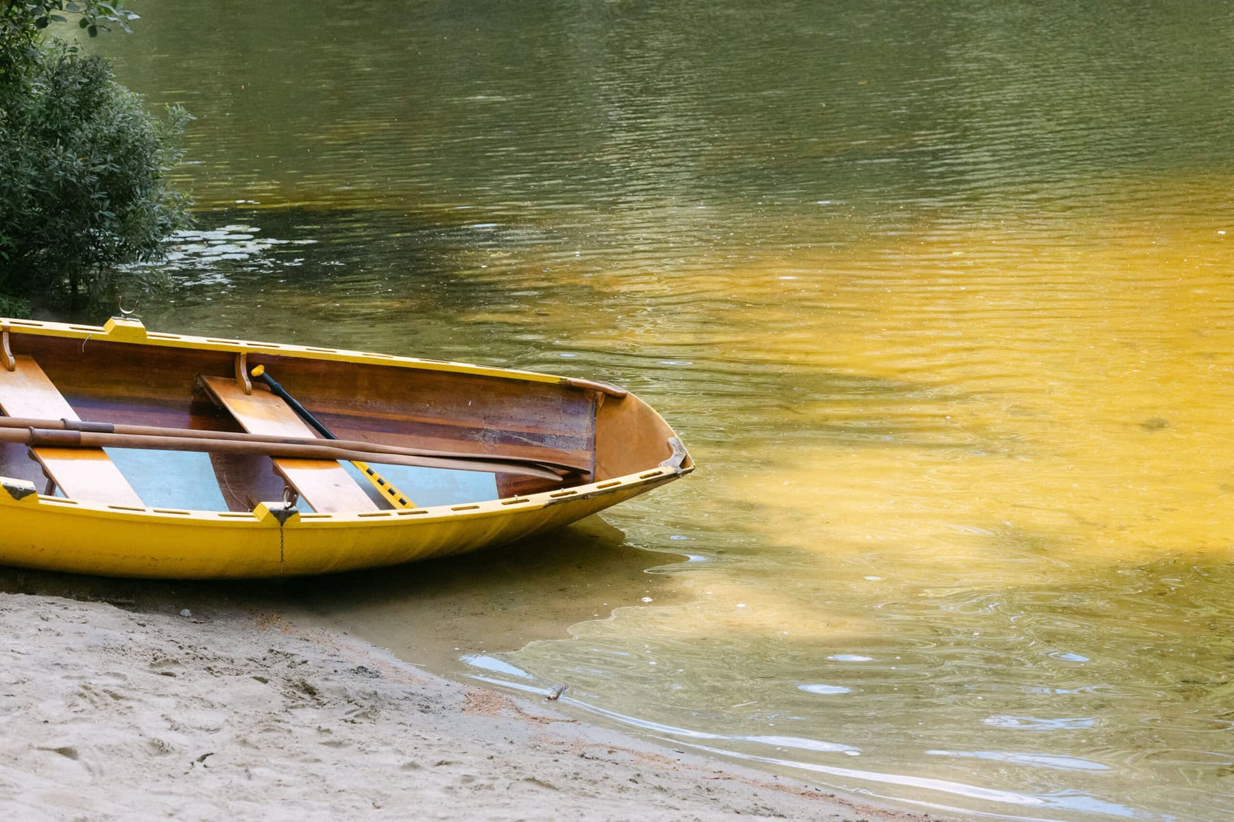 A Worcester Wedding at Cook Pond 88 A yellow rowboat rests on the sandy shore of Cook Pond, its calm waters reflecting trees—a tranquil Worcester Wedding setting.