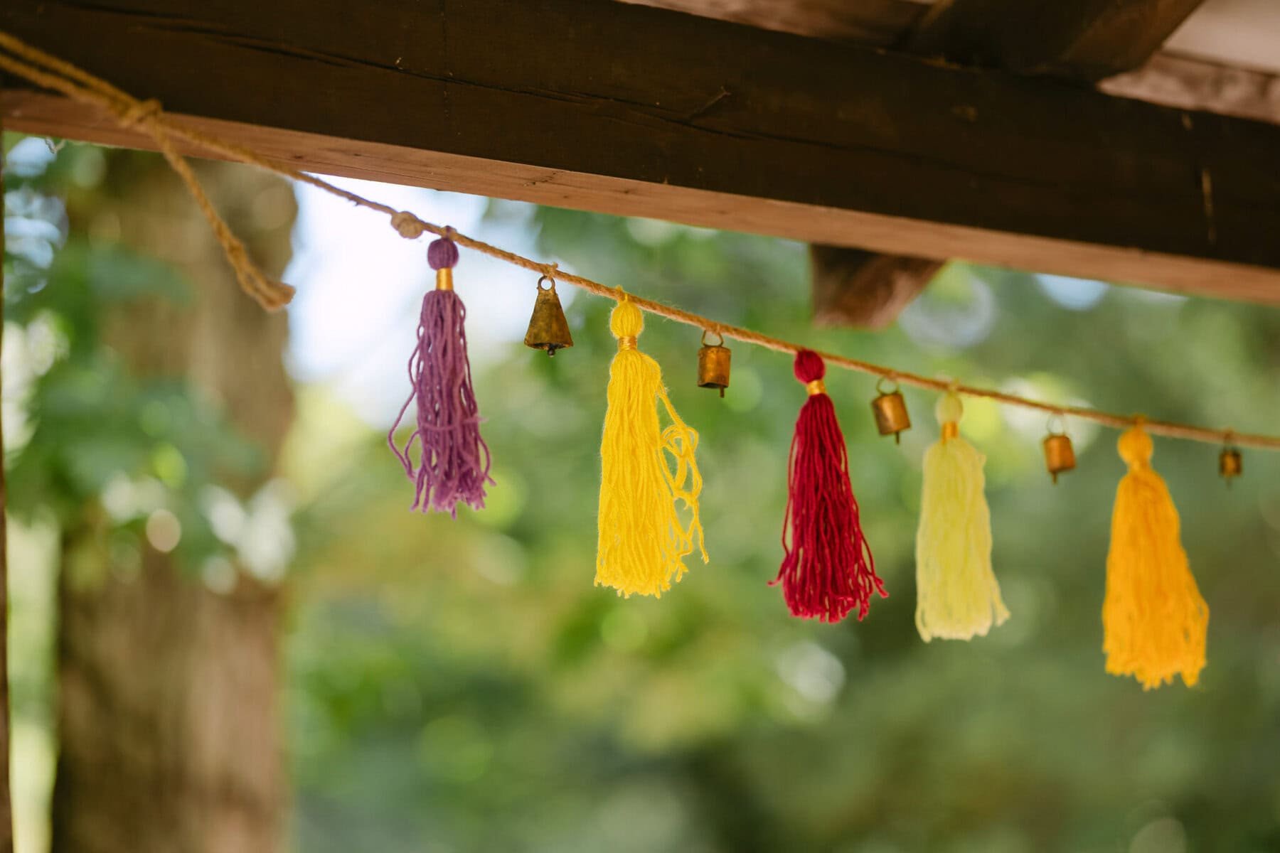 A Worcester Wedding at Cook Pond 11 A string garland with purple, yellow, and red tassels hangs at a Worcester Wedding under a wooden structure by Cook Pond.