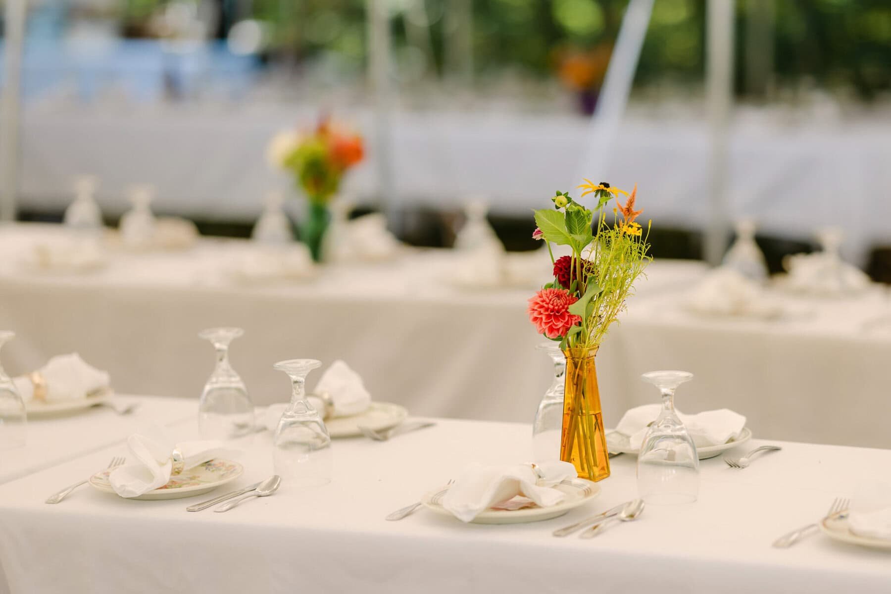 A Worcester Wedding at Cook Pond 12 A long table set with white linens, plates, and a yellow vase of flowers awaits guests at this elegant Worcester Wedding near Cook Pond.