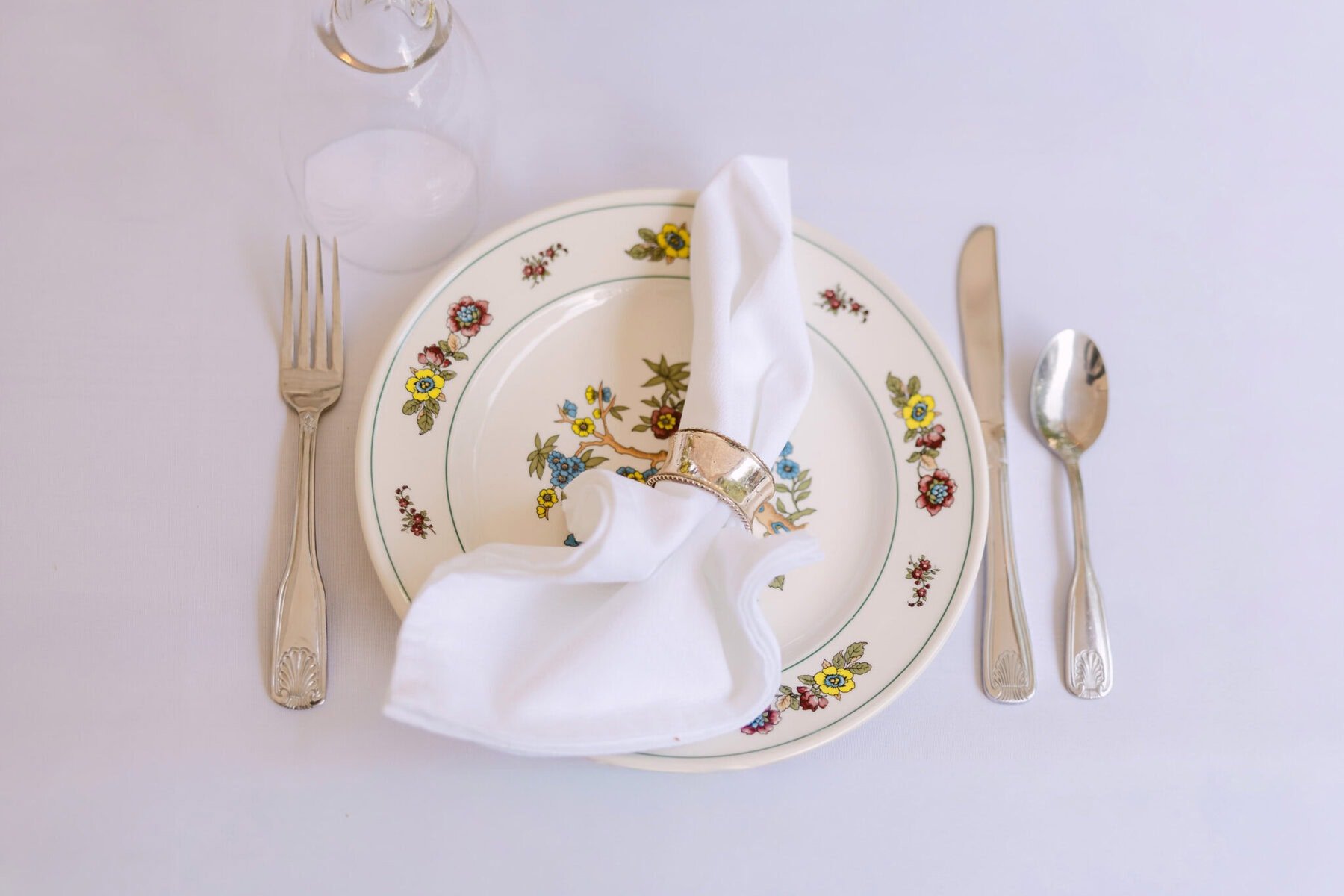 A Worcester Wedding at Cook Pond 17 A floral plate, napkin ring, and cutlery set for a Worcester wedding on a white tablecloth, ready for your special celebration.