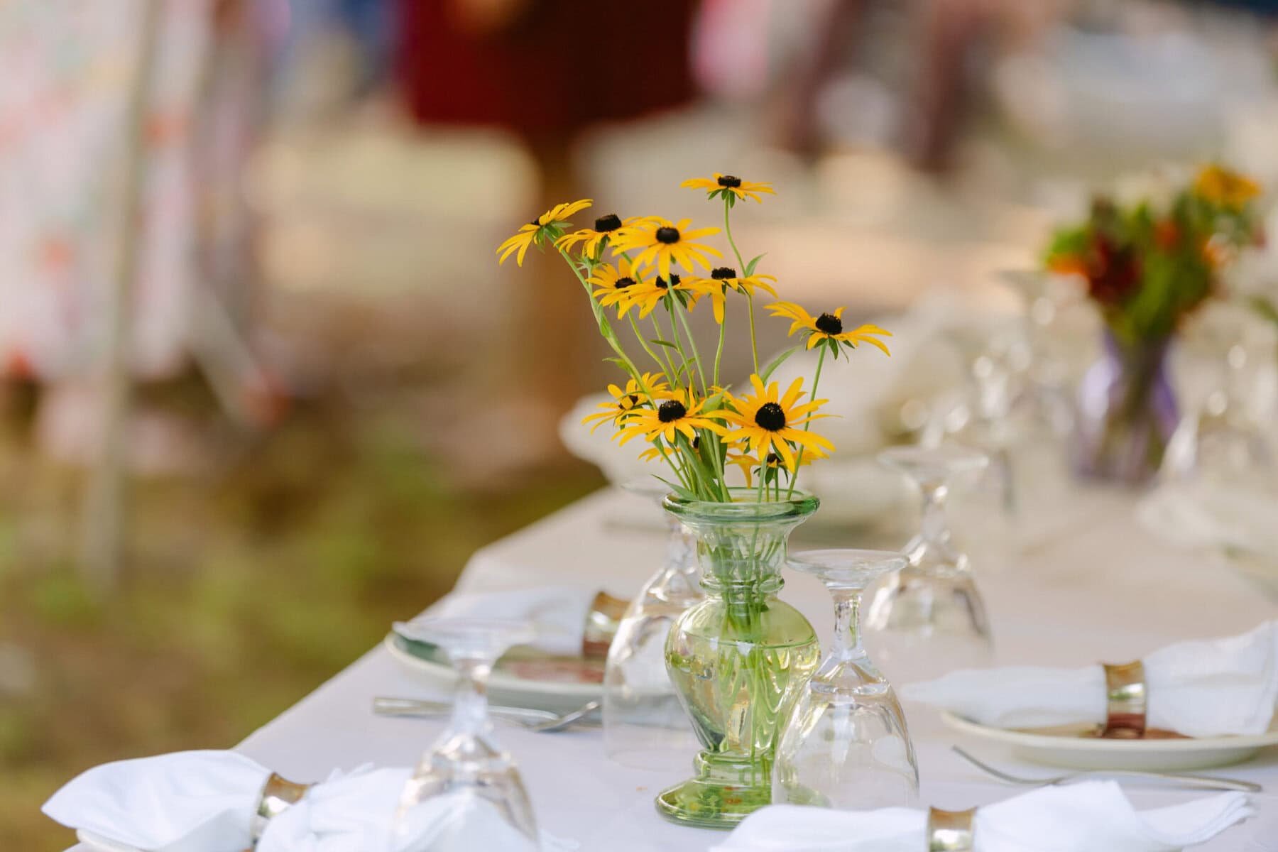 A Worcester Wedding at Cook Pond 19 A clear vase with yellow flowers sits on a set Worcester Wedding dining table, with glasses, napkins, and plates arranged neatly.
