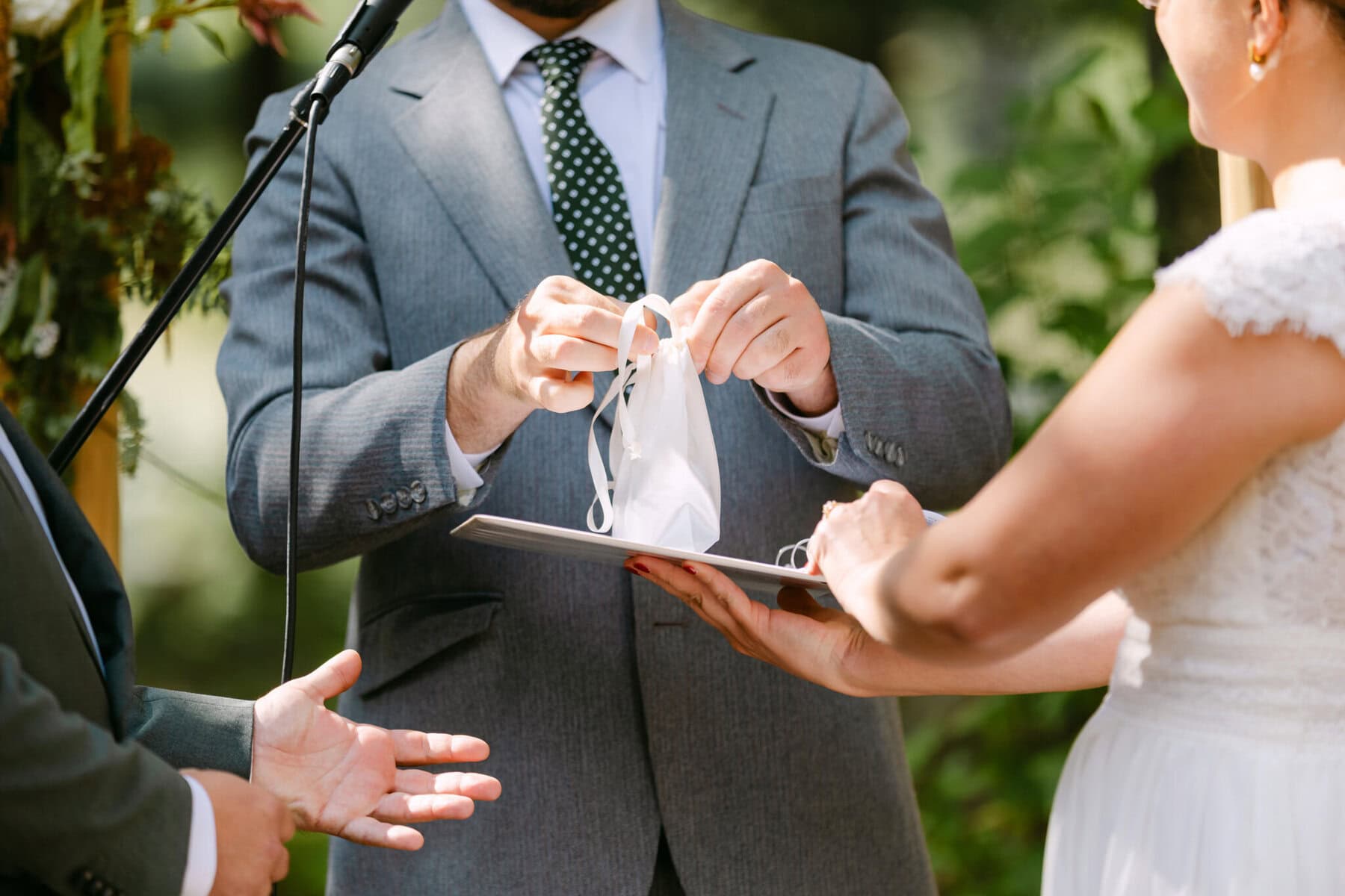 A Worcester Wedding at Cook Pond 38 At a Worcester Wedding by Cook Pond, a suited guest holds a face mask above a clipboard as another in white reviews it outdoors.