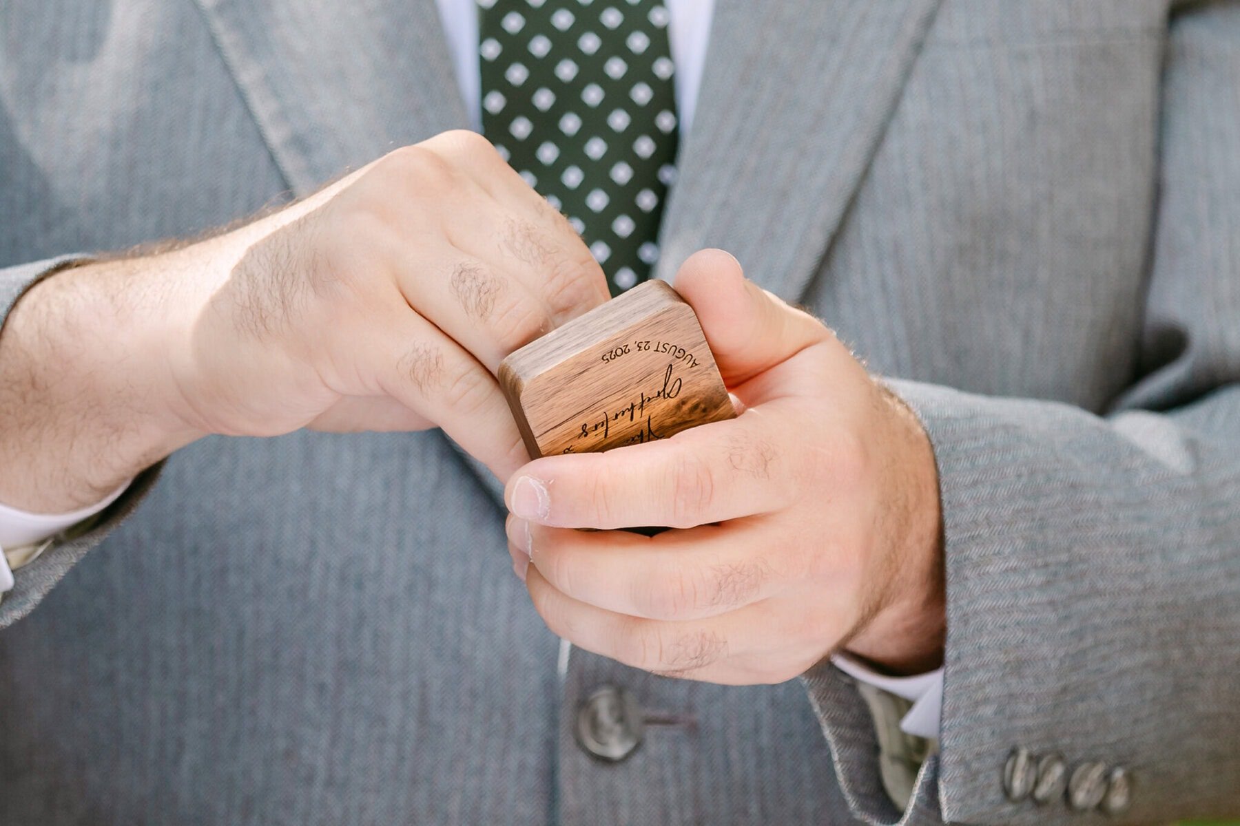 A Worcester Wedding at Cook Pond 40 A person in a gray suit holds a wooden stamp engraved with "September 13, 2023" at Worcester Wedding, pressing it onto an ink pad.