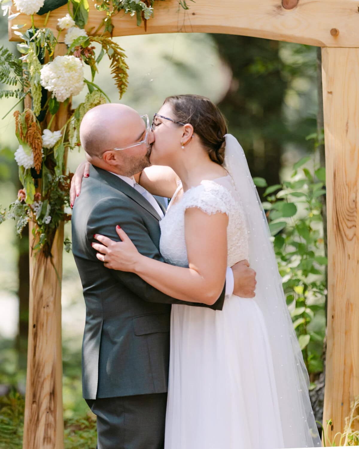 A Worcester Wedding at Cook Pond 44 A bride and groom kiss under a wooden arch adorned with flowers at their picturesque Cook Pond Worcester Wedding ceremony.