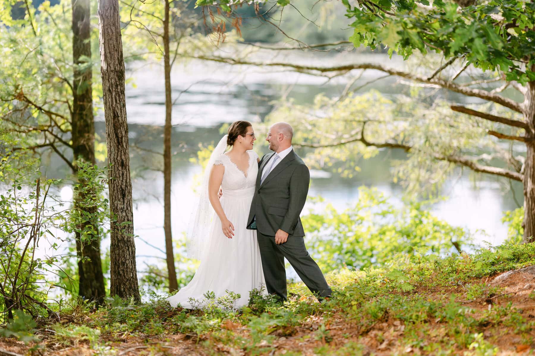 A Worcester Wedding at Cook Pond 47 A bride and groom stand facing each other outdoors near Cook Pond, surrounded by trees and greenery at their Worcester Wedding.