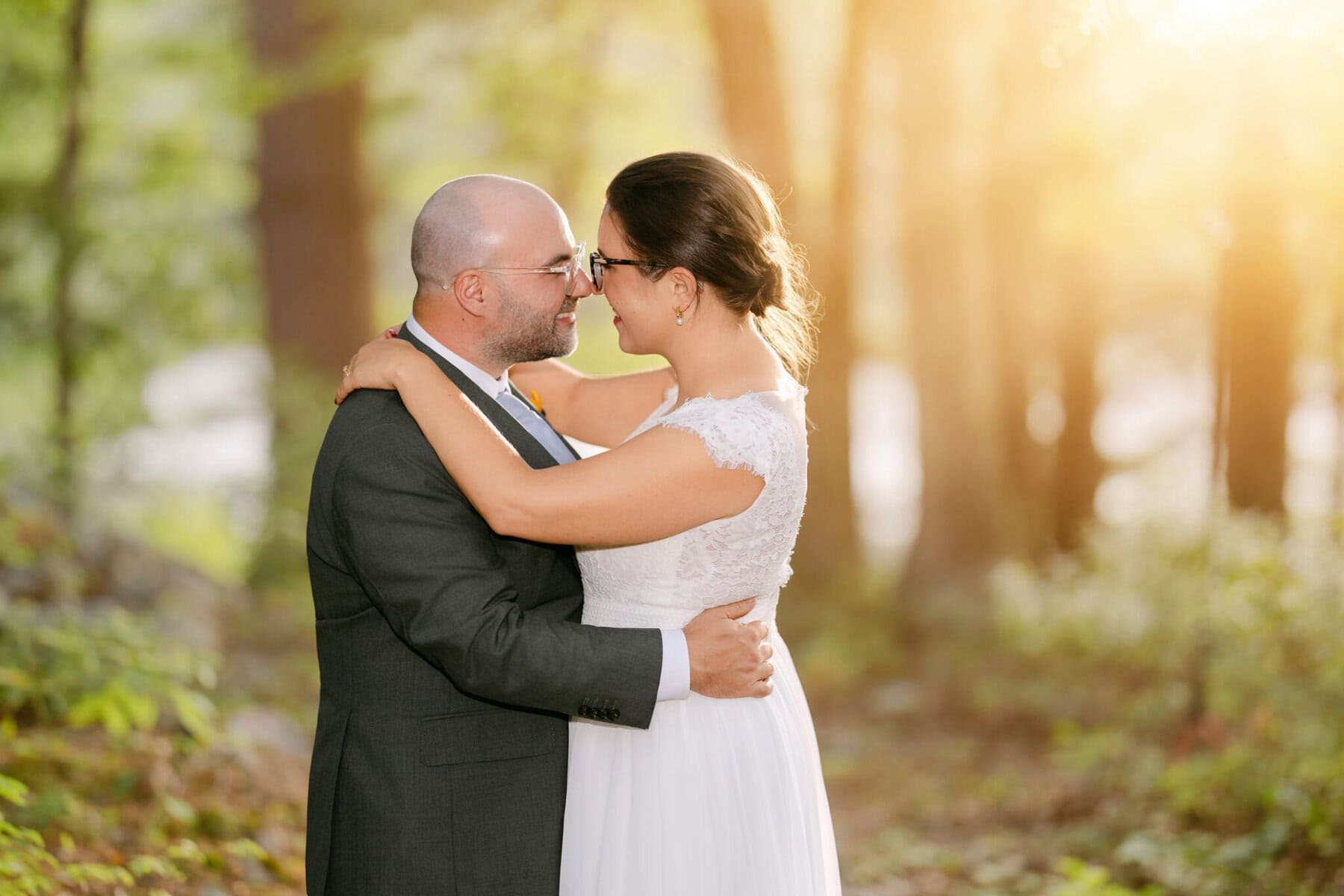 A Worcester Wedding at Cook Pond 55 A couple in wedding attire embraces by Cook Pond, gazing into each other’s eyes as sunlight illuminates their Worcester Wedding.