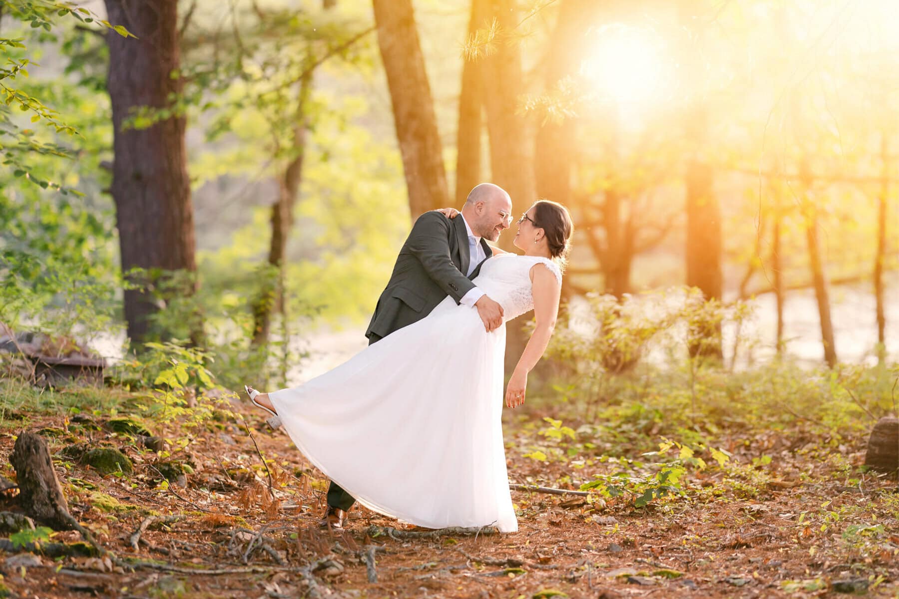 A Worcester Wedding at Cook Pond 56 A man in a suit dips a woman in a white dress outdoors at a sunlit Worcester Wedding amid trees and greenery.
